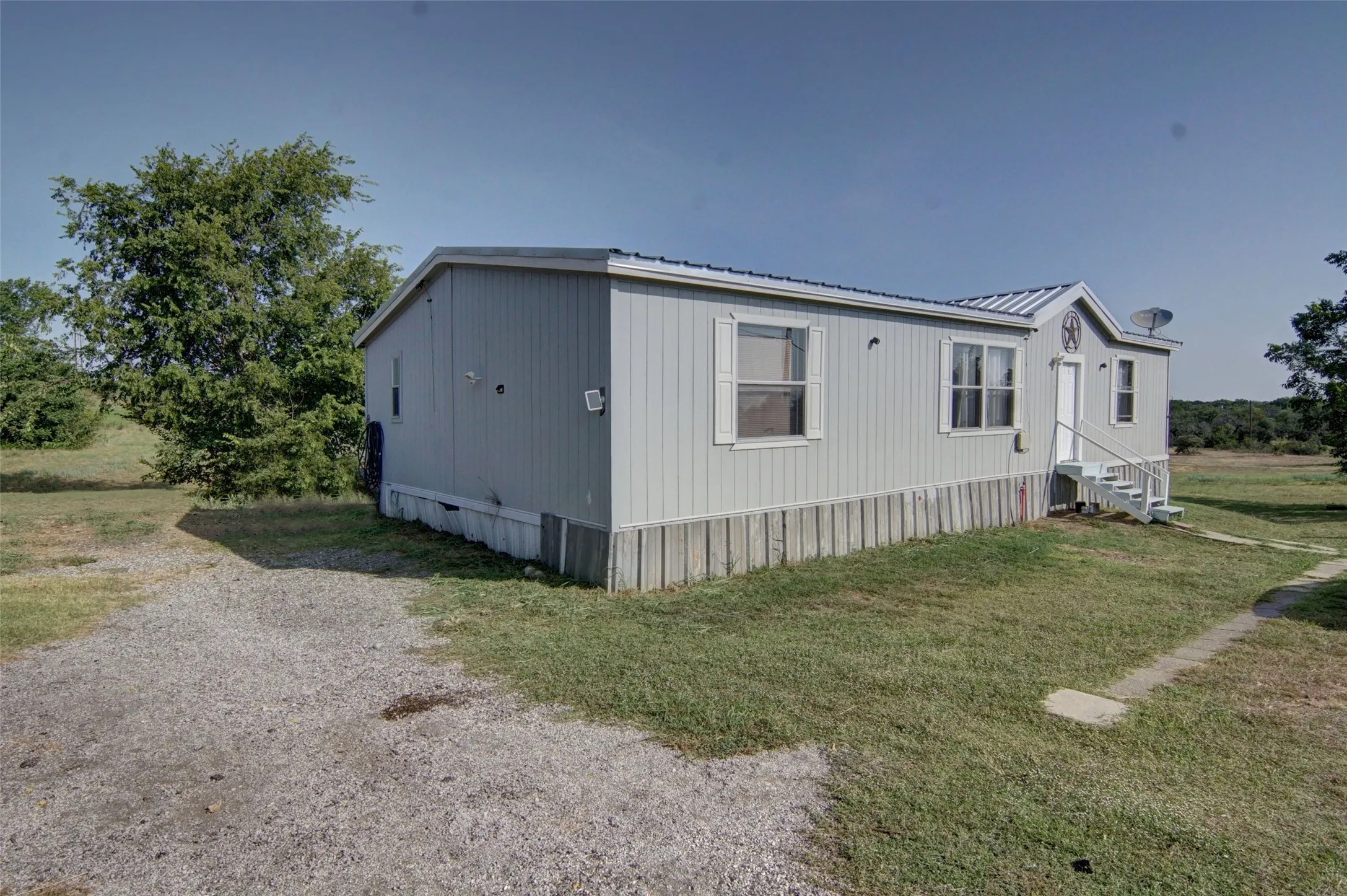 Single-story residence featuring light gray siding, white window trim, and a gravel driveway