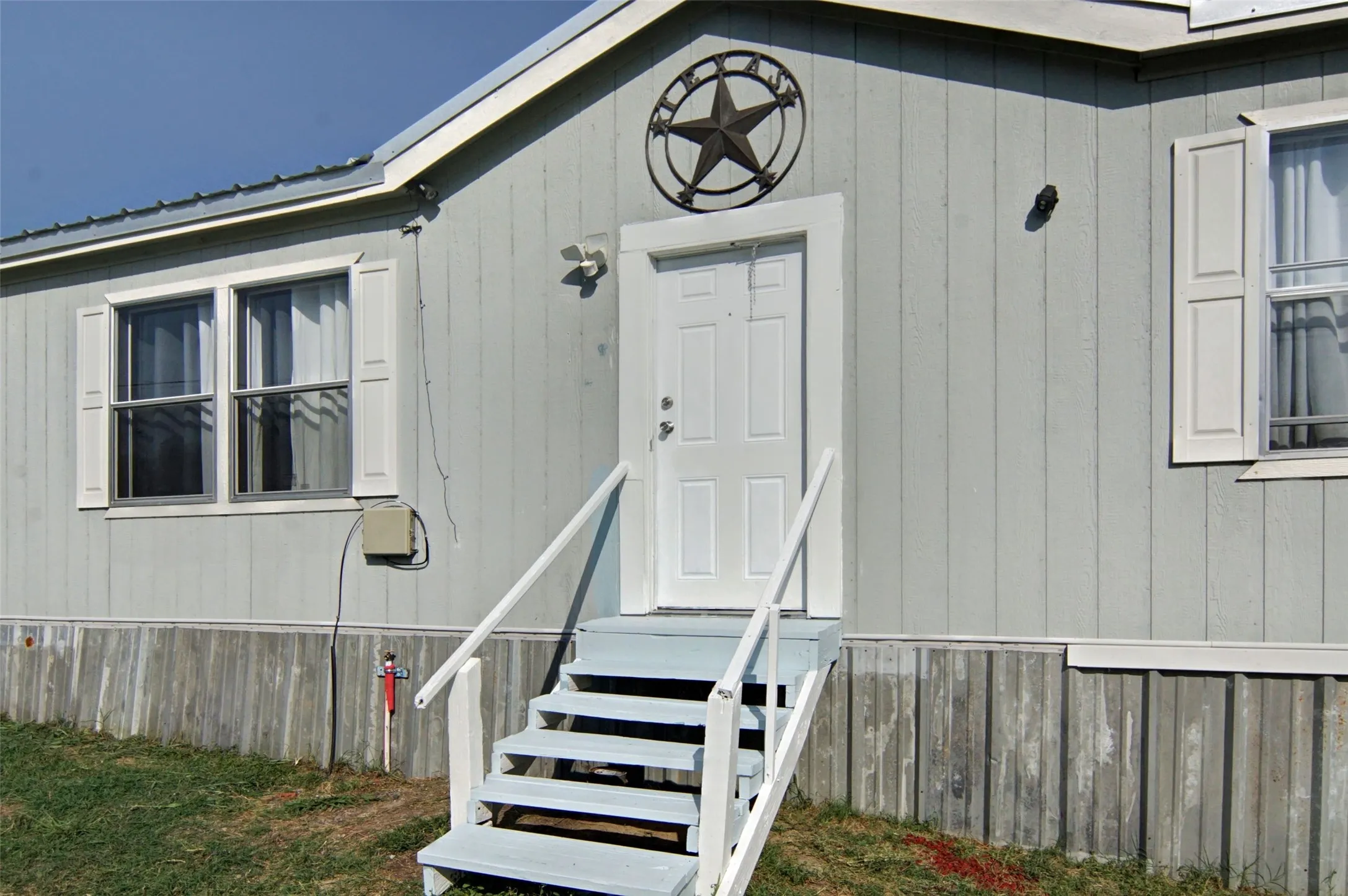 Exterior featuring light-gray vertical siding, white trim, and a white entry door with a multi-pane design