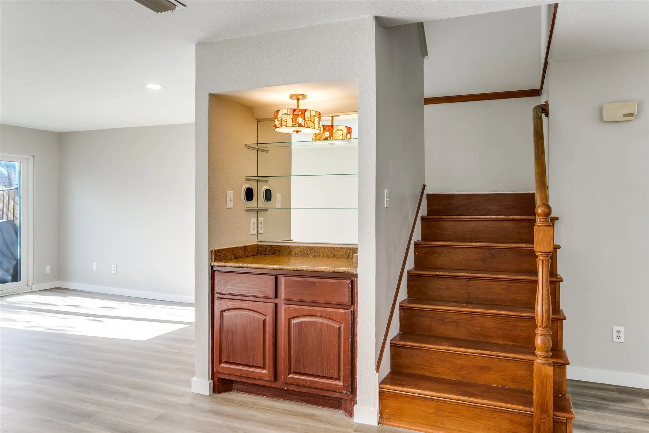 Built-in wet bar featuring a polished countertop, glass shelving, and an overhead decorative light fixture