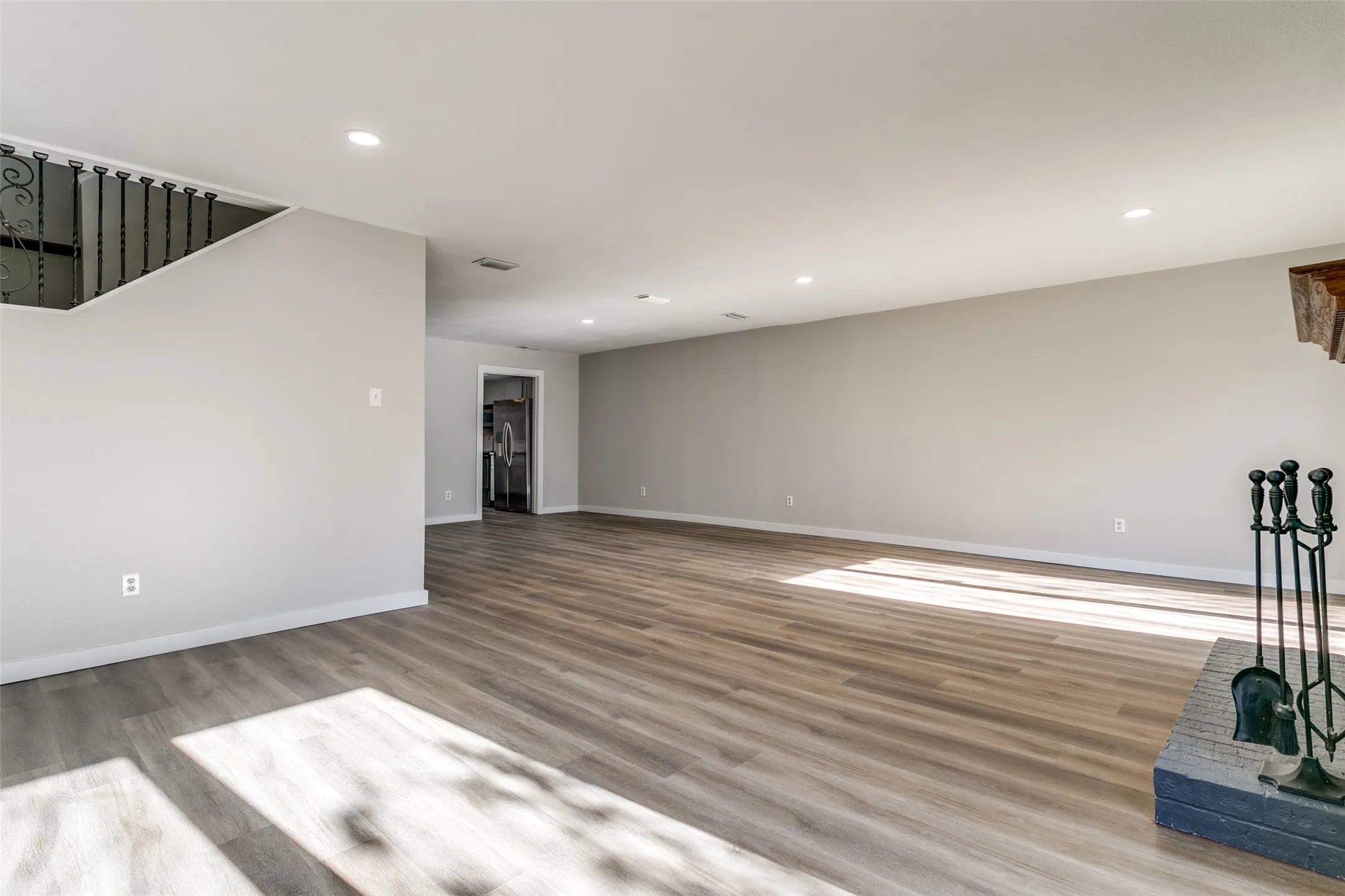 Spacious living area featuring wood-finish flooring, recessed lighting, neutral wall tones, and a staircase with wrought iron balusters