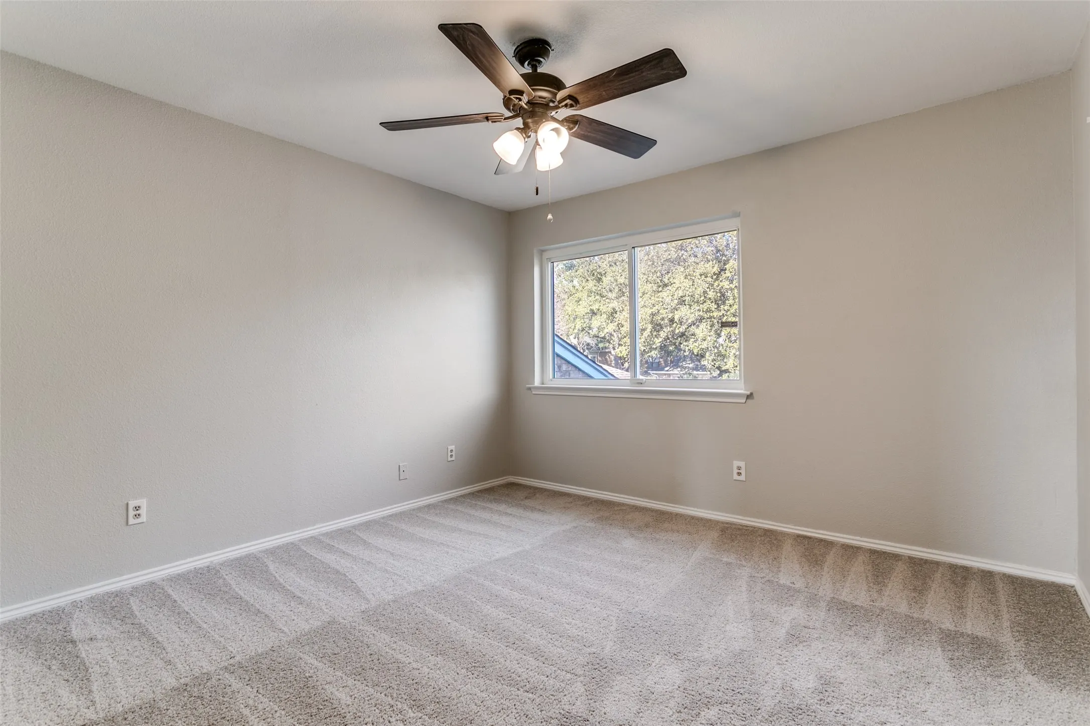 Neutral-toned room featuring a ceiling fan with light fixture, double-pane window, light-colored walls, and patterned carpeting