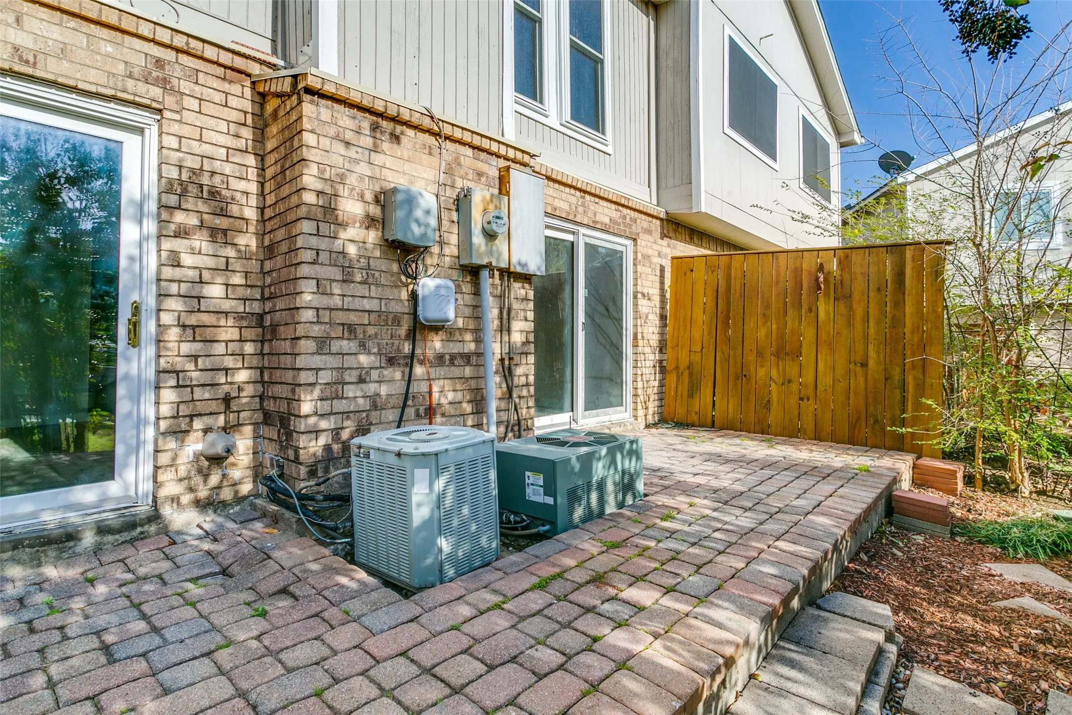 Brick paver patio featuring a wood privacy fence and two external AC units
