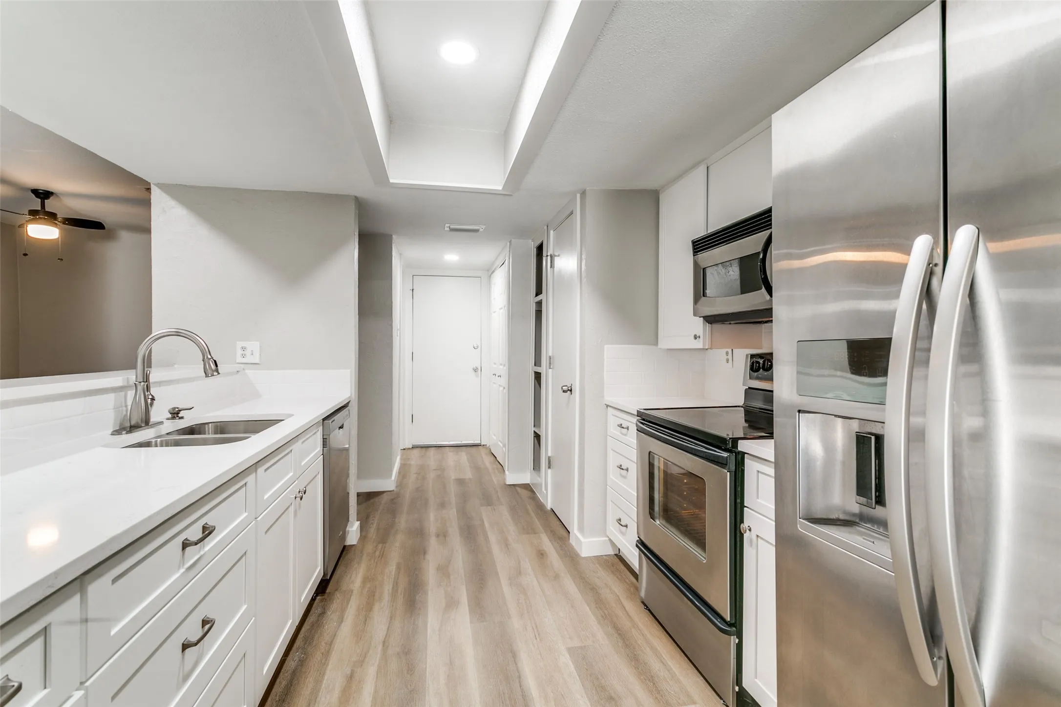 Galley kitchen featuring white cabinetry, light countertops, wood-finish flooring, stainless steel appliances, and recessed lighting