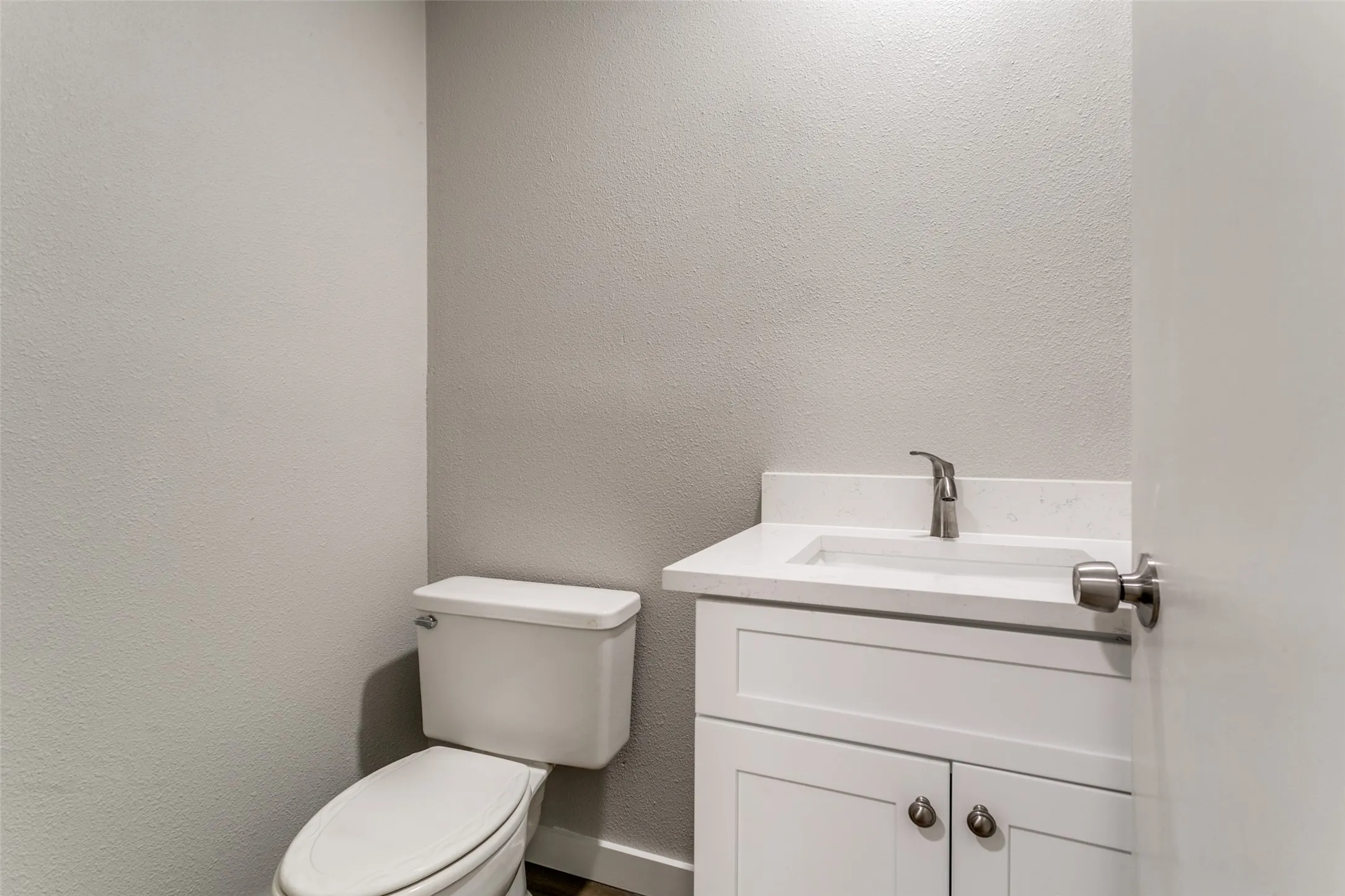 Powder room featuring a white single-sink vanity with a light-toned countertop, a contemporary brushed nickel faucet, and a white toilet