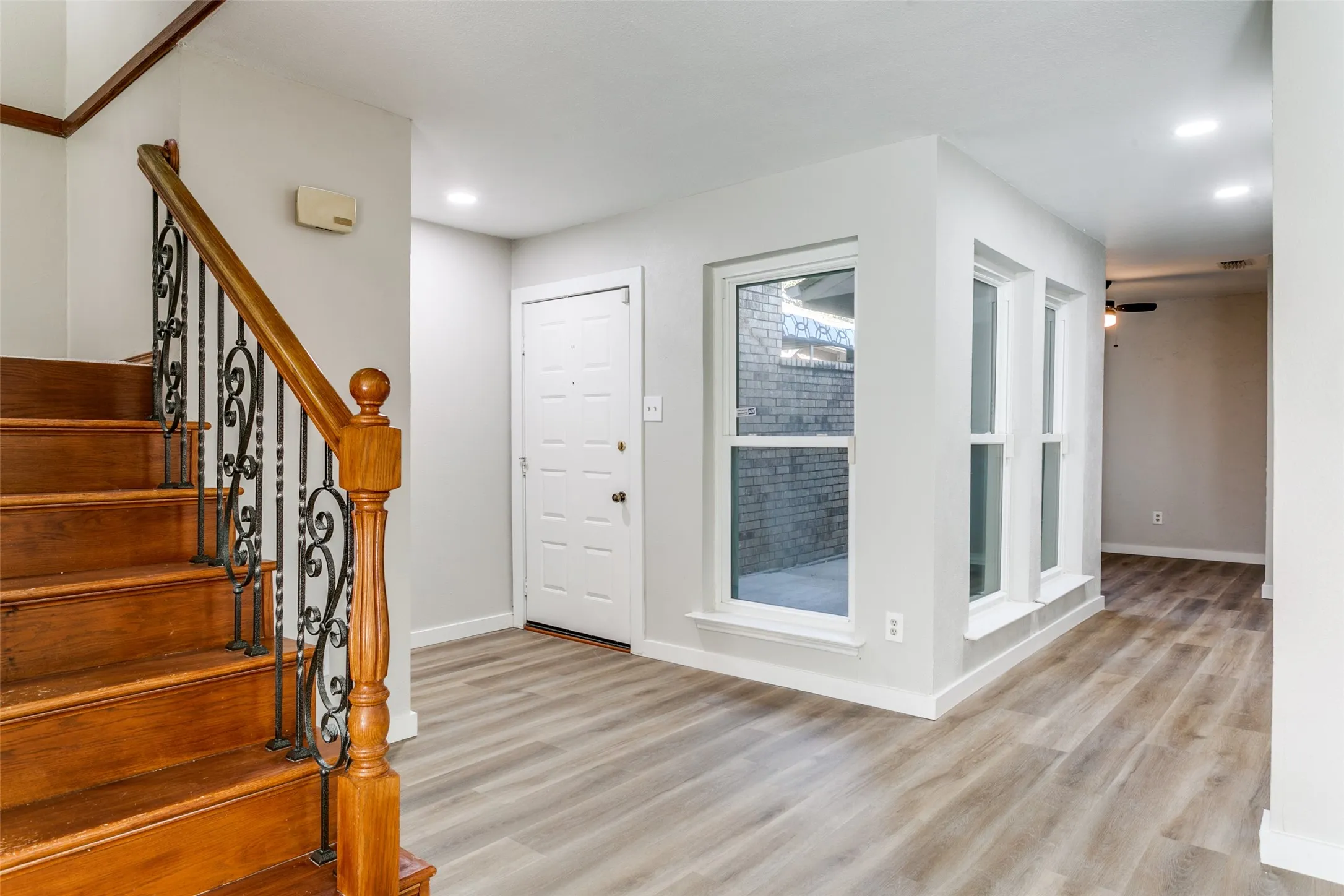 Entryway featuring wood-finish flooring, a wood staircase with wrought iron balusters, multiple windows, and recessed lighting