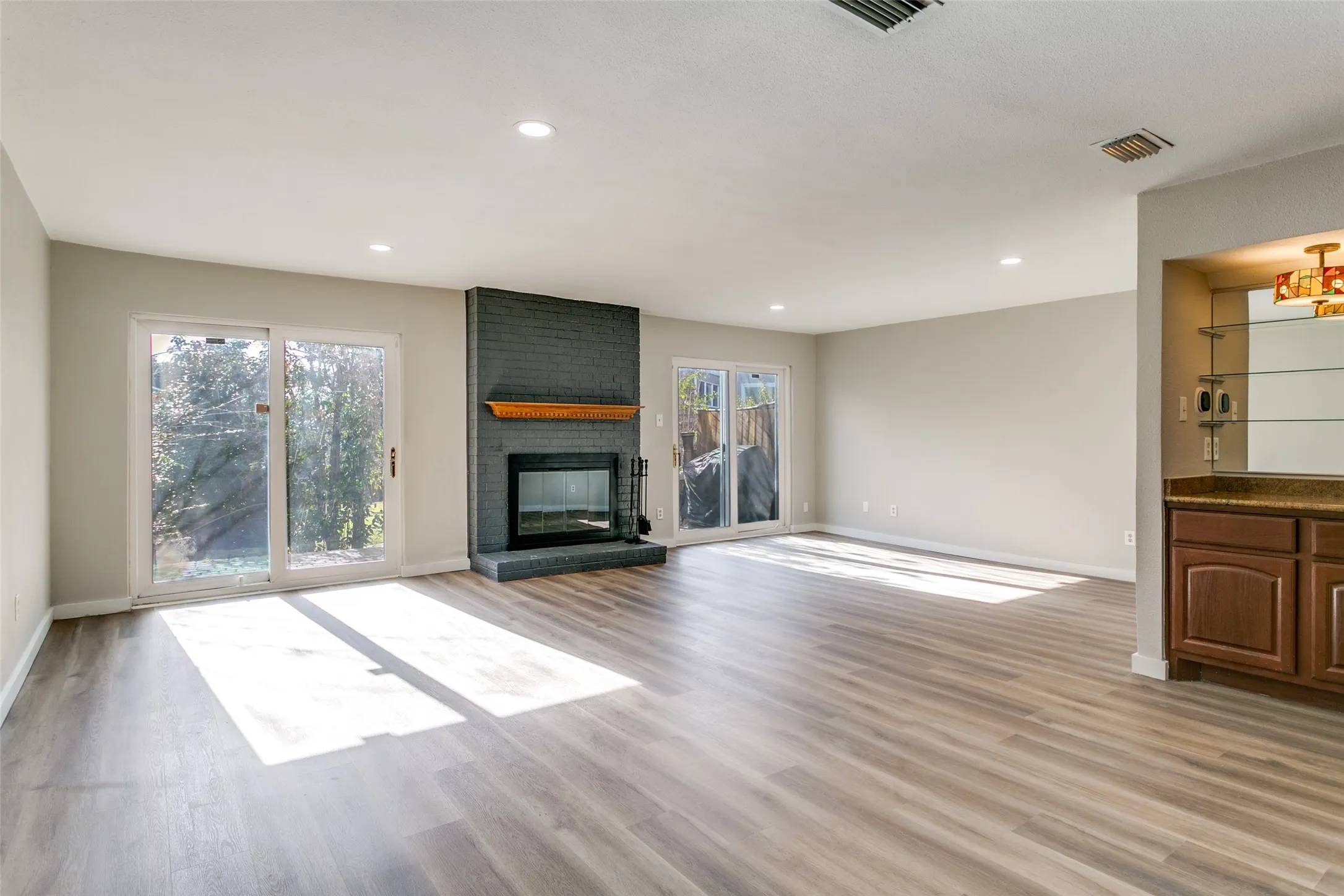 Spacious living area featuring wood-finish flooring, a contemporary dark brick fireplace with a wood mantel, and two sets of sliding glass doors