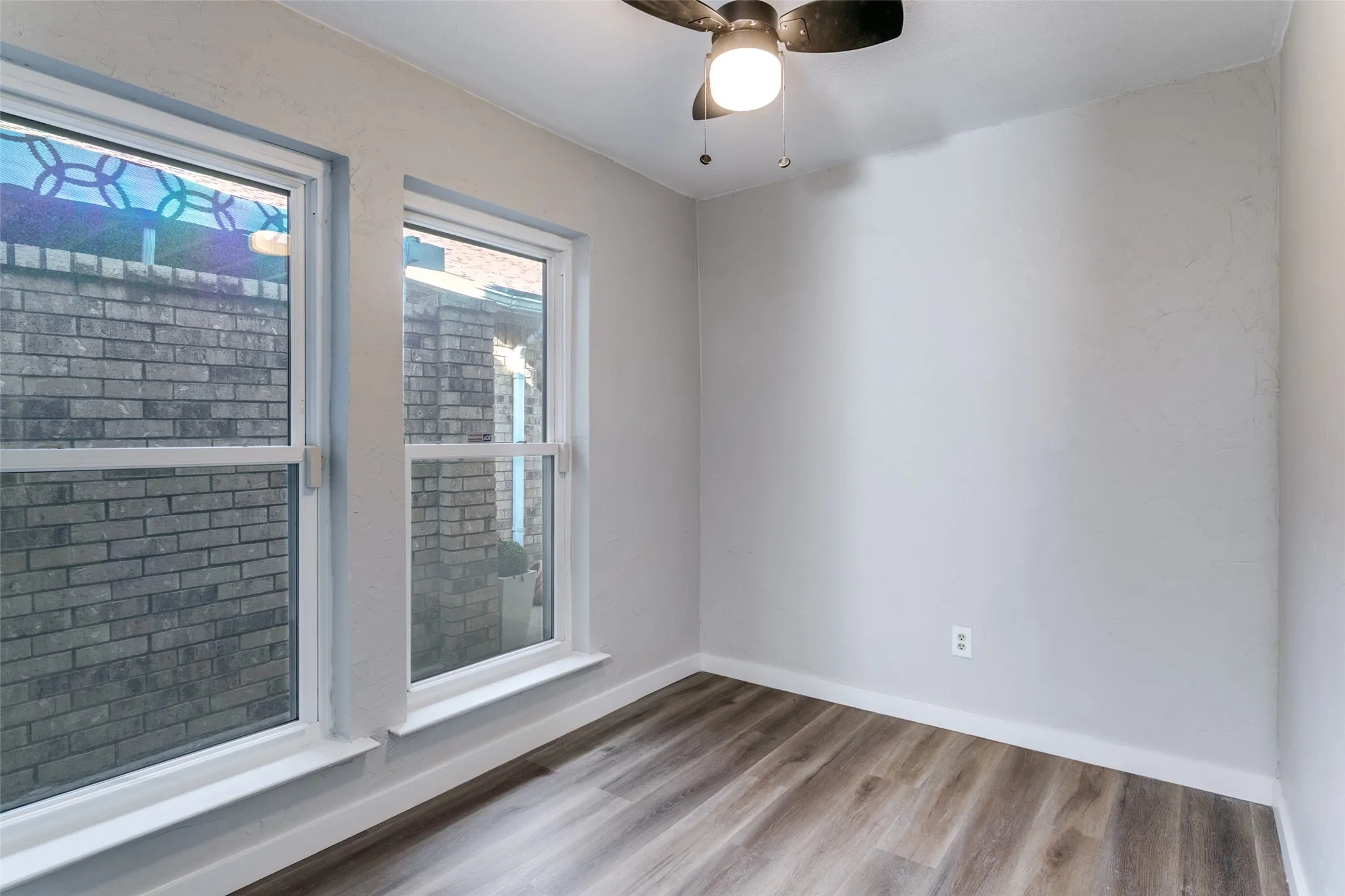 Bright room with two windows, wood-finish flooring, and a ceiling fan with integrated lighting