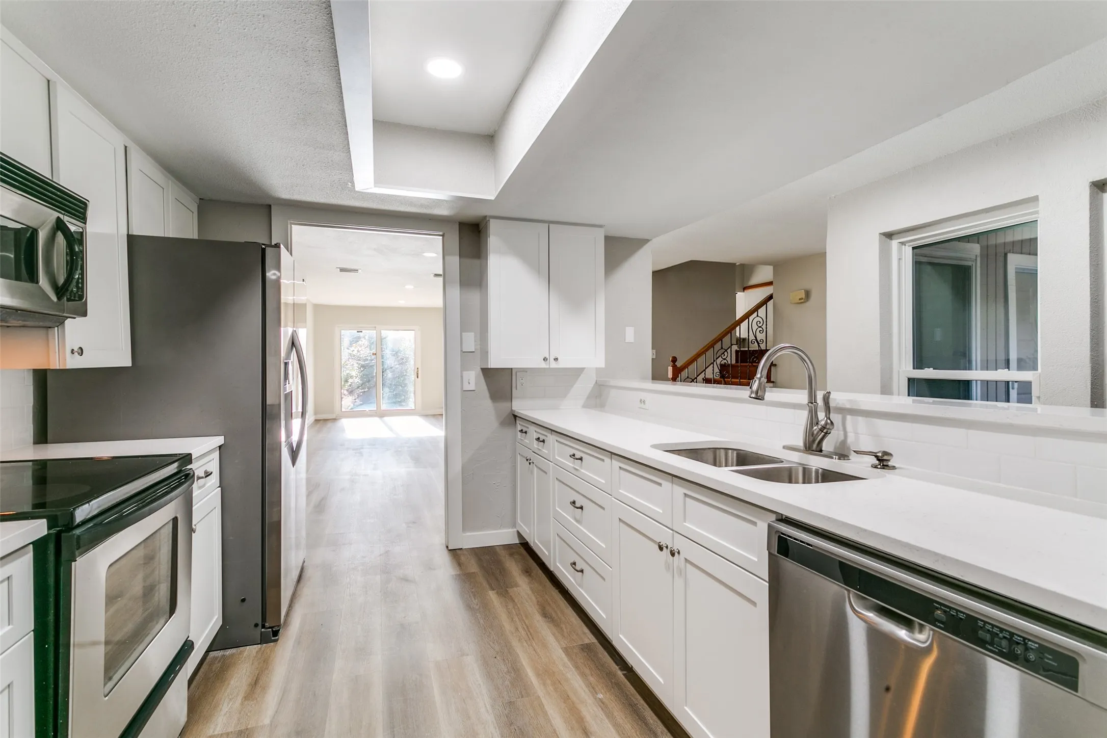 Kitchen featuring white shaker cabinetry, stainless steel appliances, wood-finish flooring, recessed lighting, and a dual basin sink with a gooseneck faucet