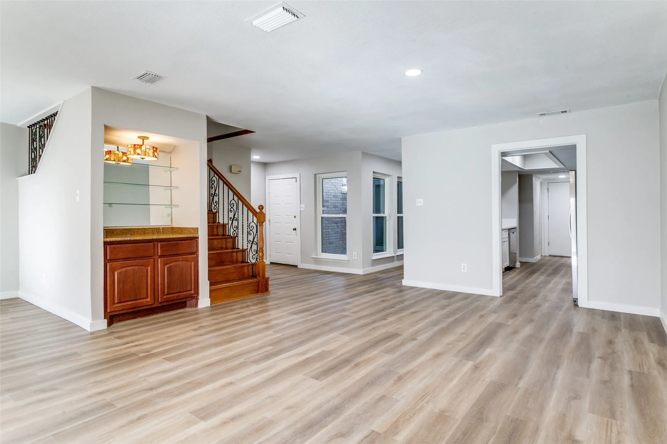 Open concept living area with wood-finish flooring, recessed lighting, and a built-in wet bar featuring wood cabinetry, a stone-look countertop, and glass shelving