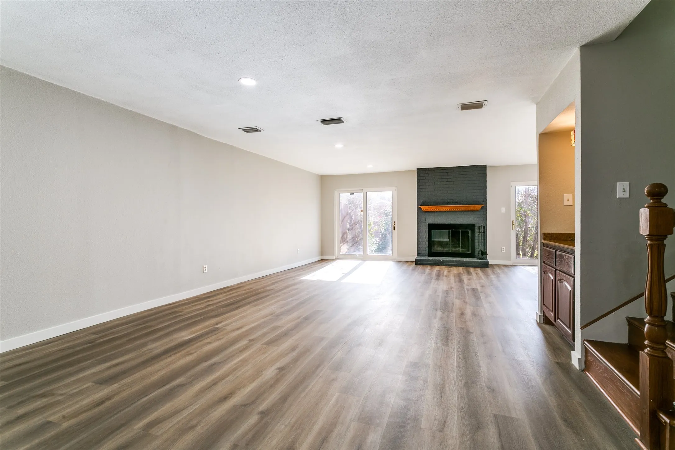 Spacious living area featuring wood-finish flooring and a fireplace with a dark brick surround and wood mantel