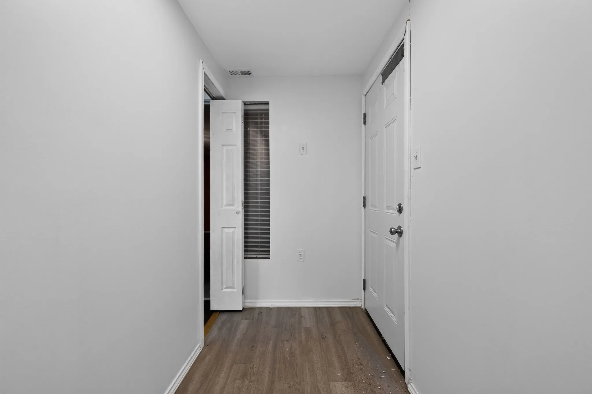 Hallway featuring wood-finish flooring, light neutral wall tones, a paneled door, and window with blinds