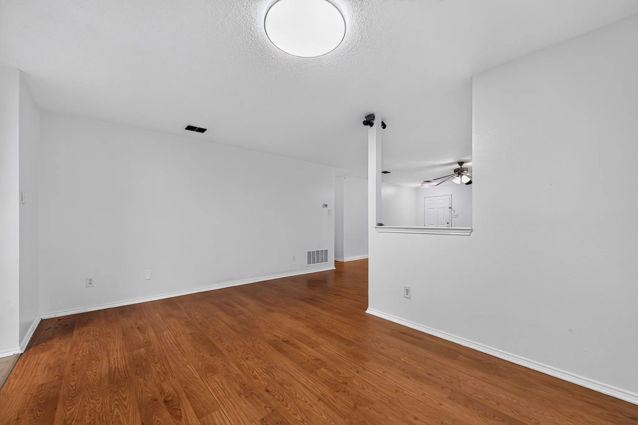Spacious room featuring wood-finish flooring, white walls, and a circular flush-mount ceiling light