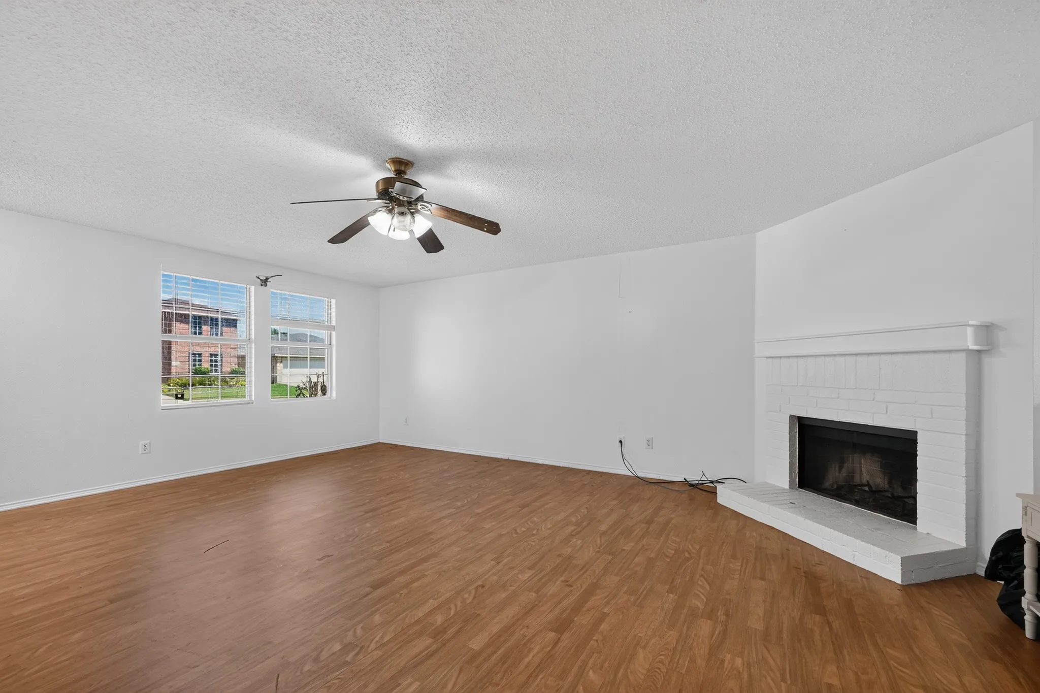 Spacious interior featuring wood-finish flooring, a ceiling fan with integrated lighting, and white walls