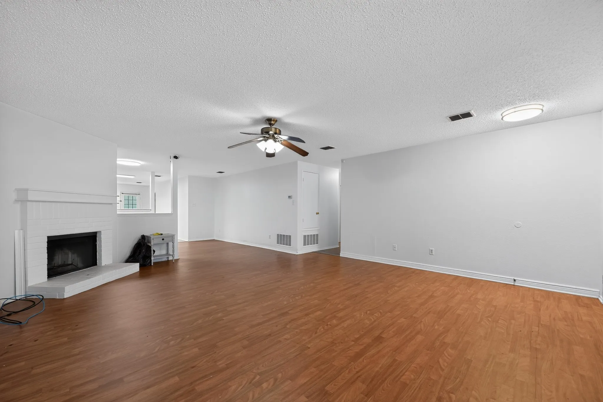 Spacious living area featuring wood-finish flooring, a white brick fireplace with a hearth, a ceiling fan, and recessed lighting