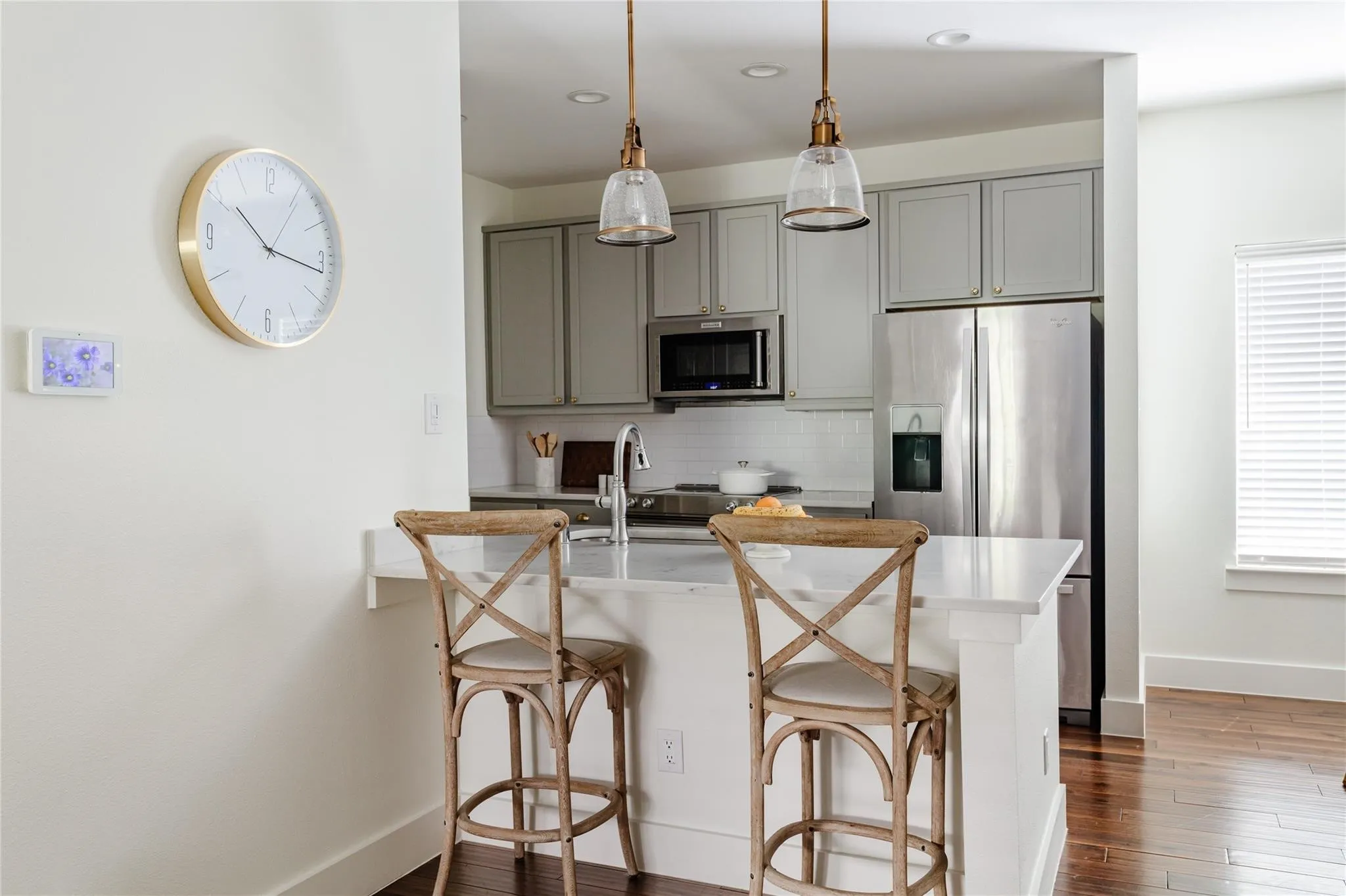 Modern kitchen featuring light gray cabinetry, stainless steel appliances, a white subway tile backsplash, and a breakfast bar with pendant lighting