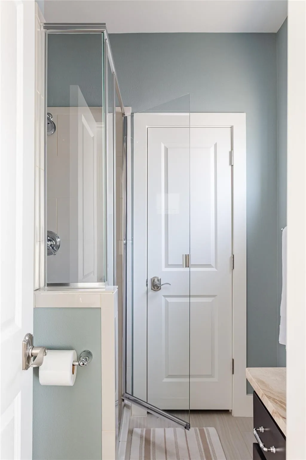 Glass-enclosed shower with chrome fixtures, white subway tile surround, and light blue wall paint