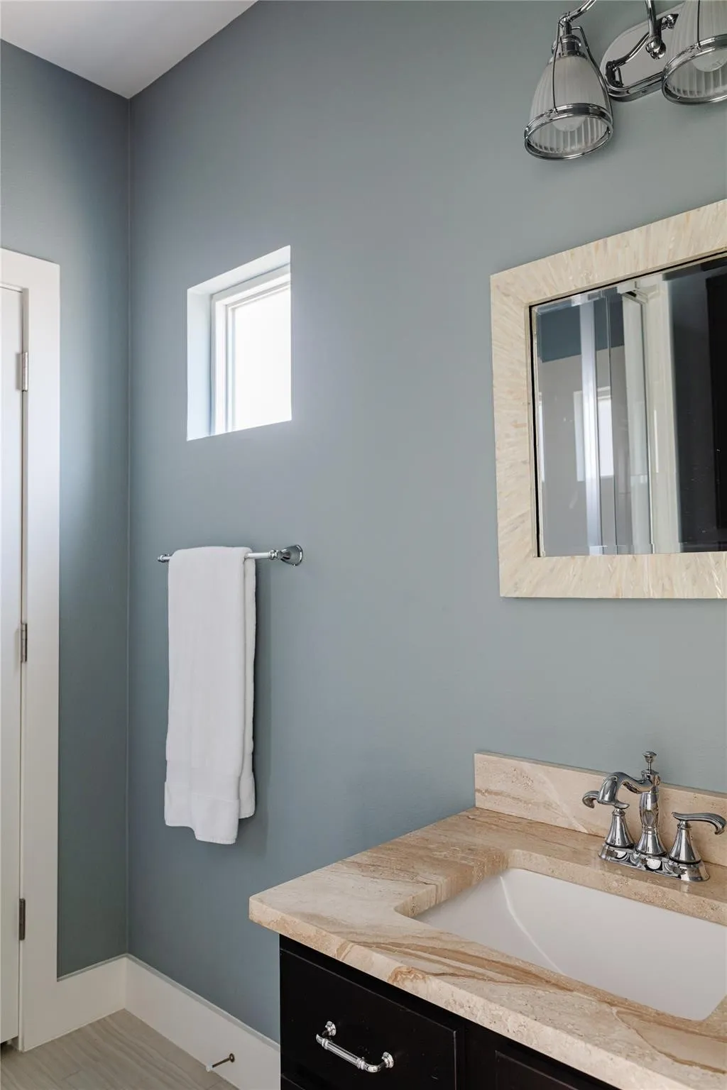 Bathroom vanity featuring a light-toned stone countertop with an integrated sink and chrome faucet