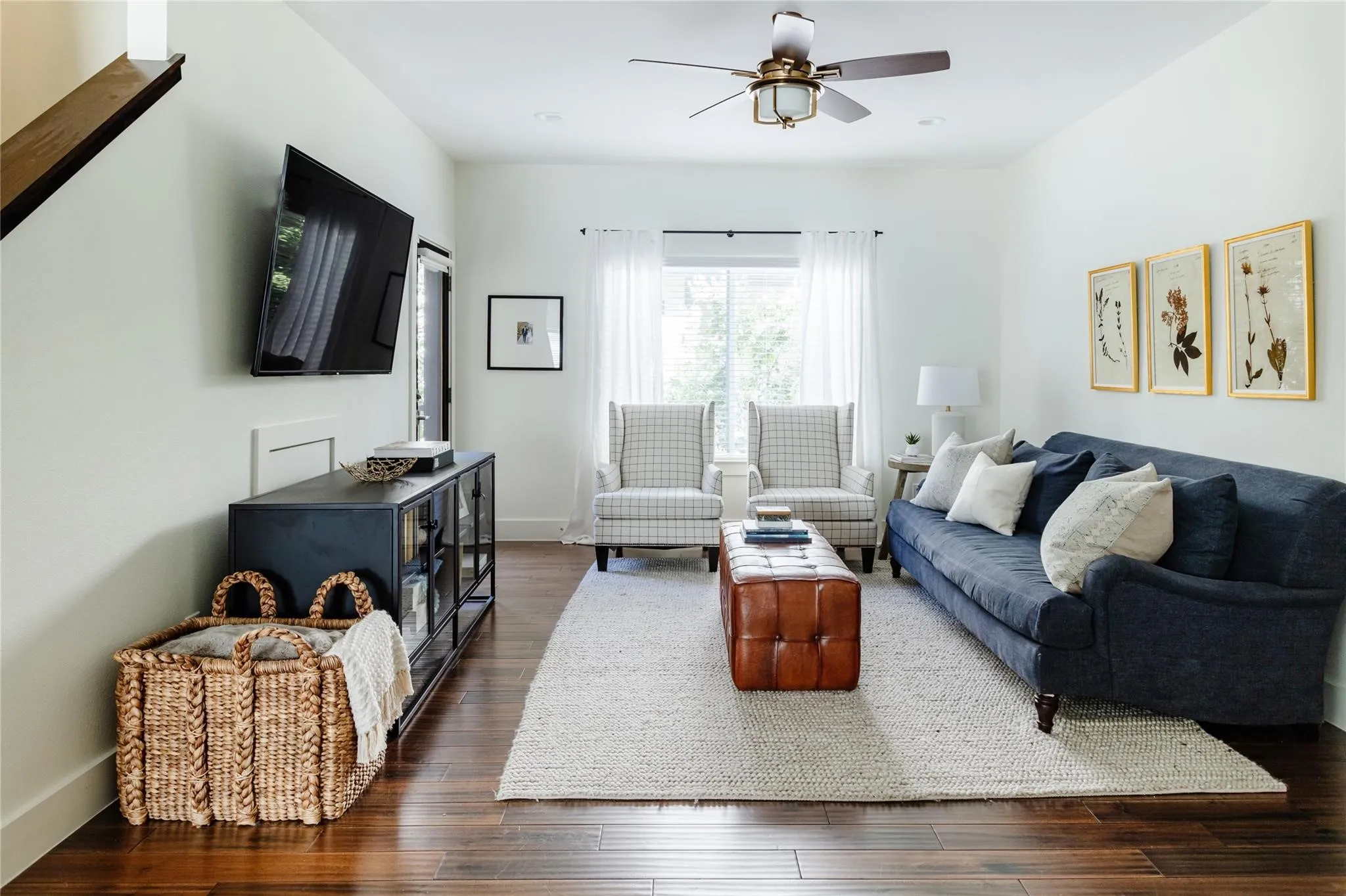 Bright living area featuring wood-finish flooring, white walls, and a ceiling fan with integrated lighting