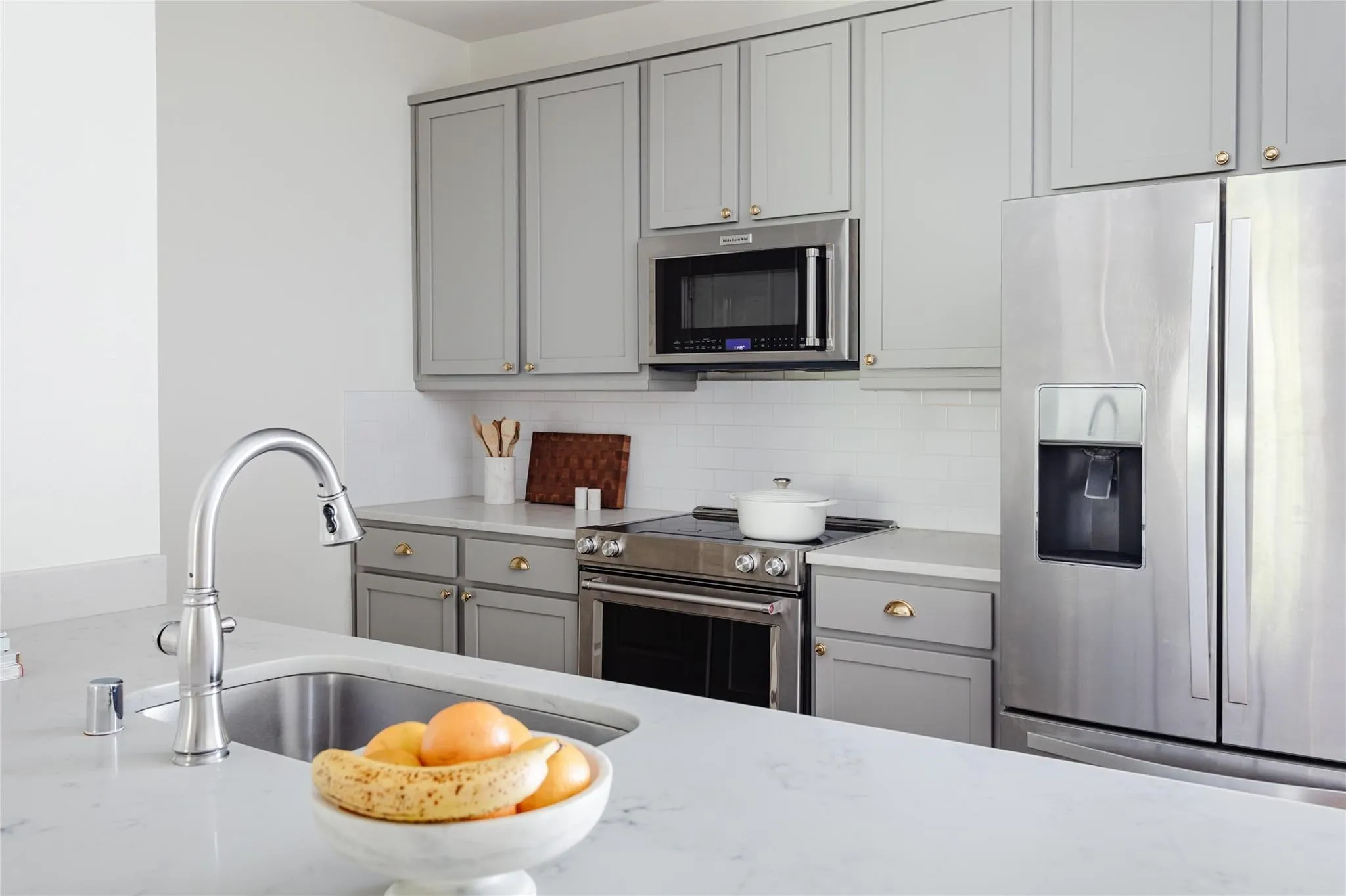 Kitchen featuring light gray cabinetry with brass hardware, stainless steel appliances, white subway tile backsplash, and light-colored countertops