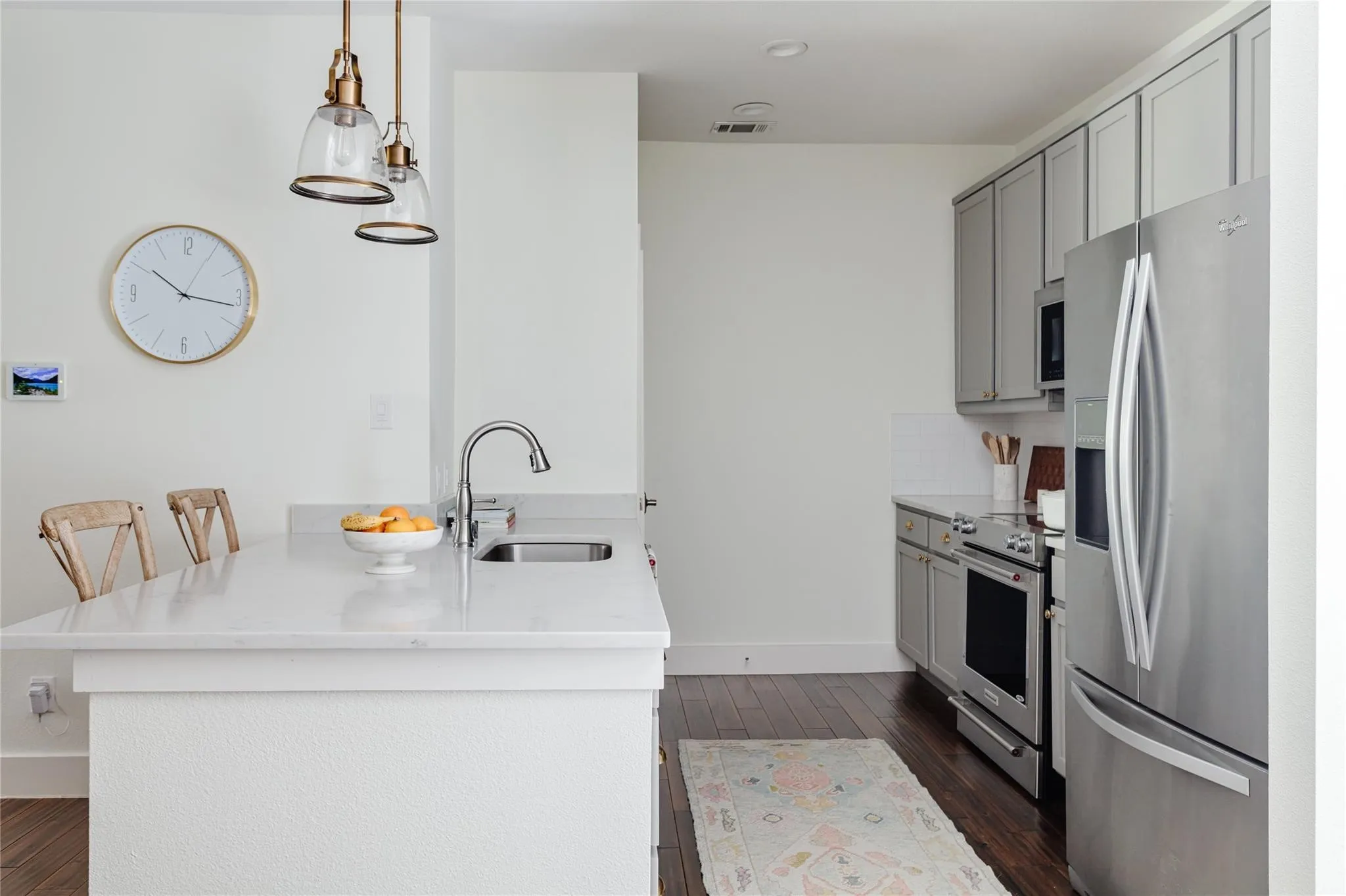 Kitchen featuring a large central island with an undermount sink, quartz countertops, pendant lighting, stainless steel appliances, and wood-finish flooring