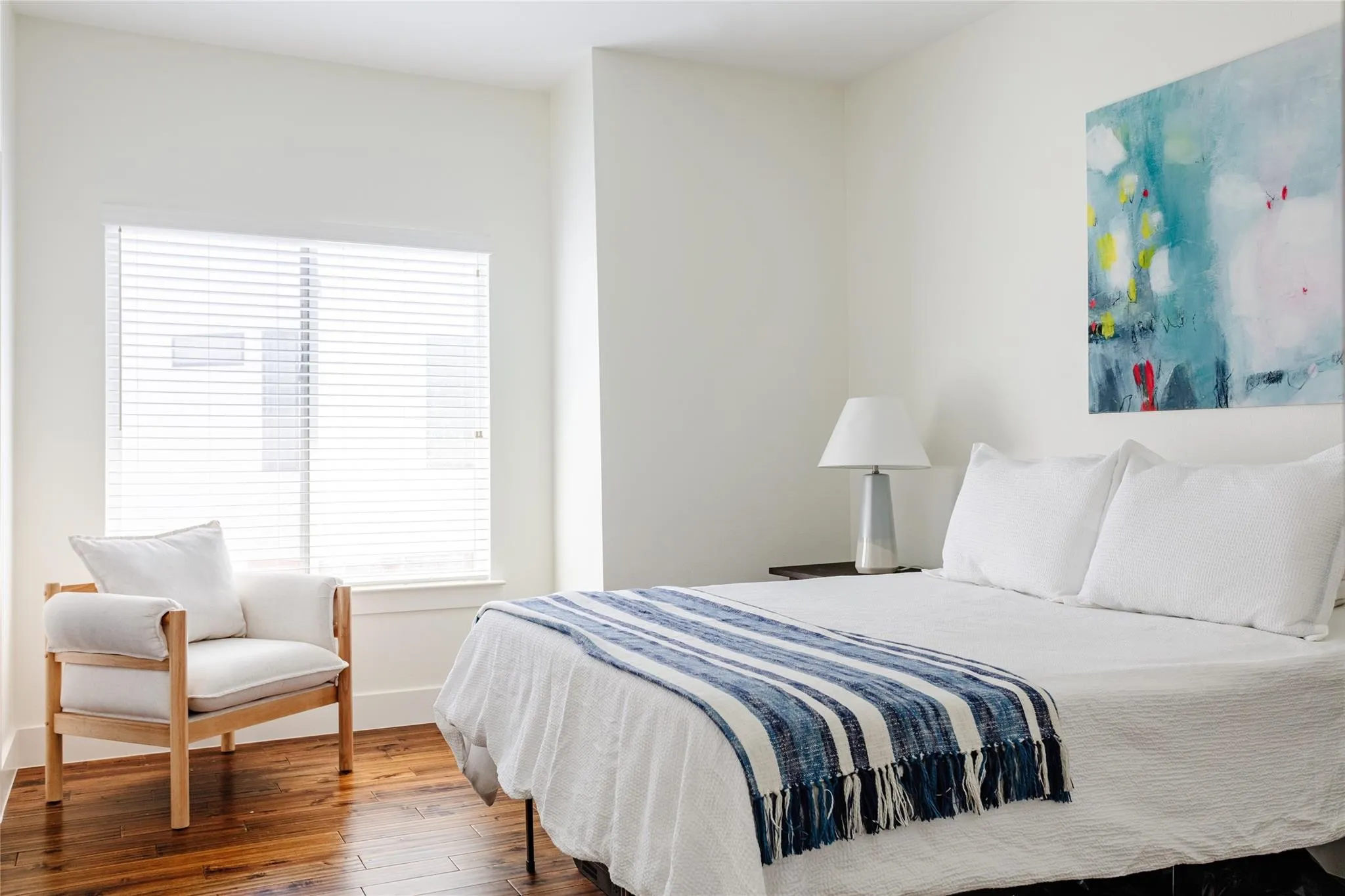 Spacious room featuring a large window with horizontal blinds, rich wood-finish flooring, and light-toned walls