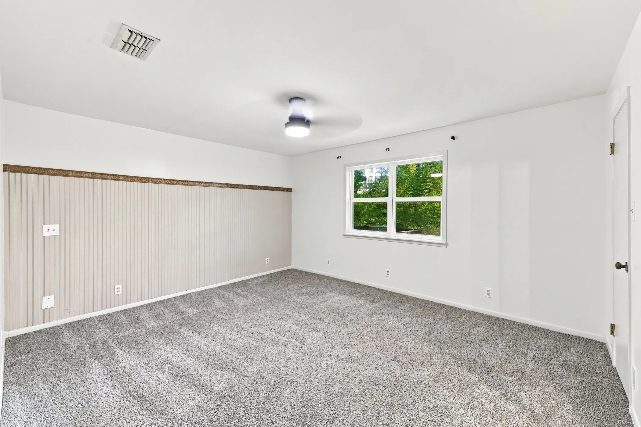 Spacious room featuring gray carpet flooring, white walls, and a modern ceiling fan with integrated lighting