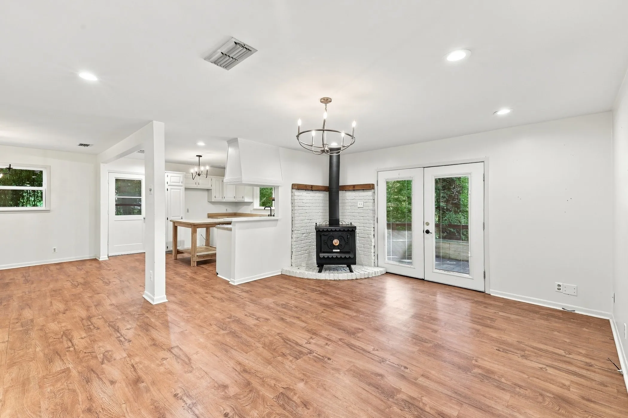 Open-concept living area featuring wood-finish flooring, a freestanding wood-burning stove with a white brick surround, and French doors