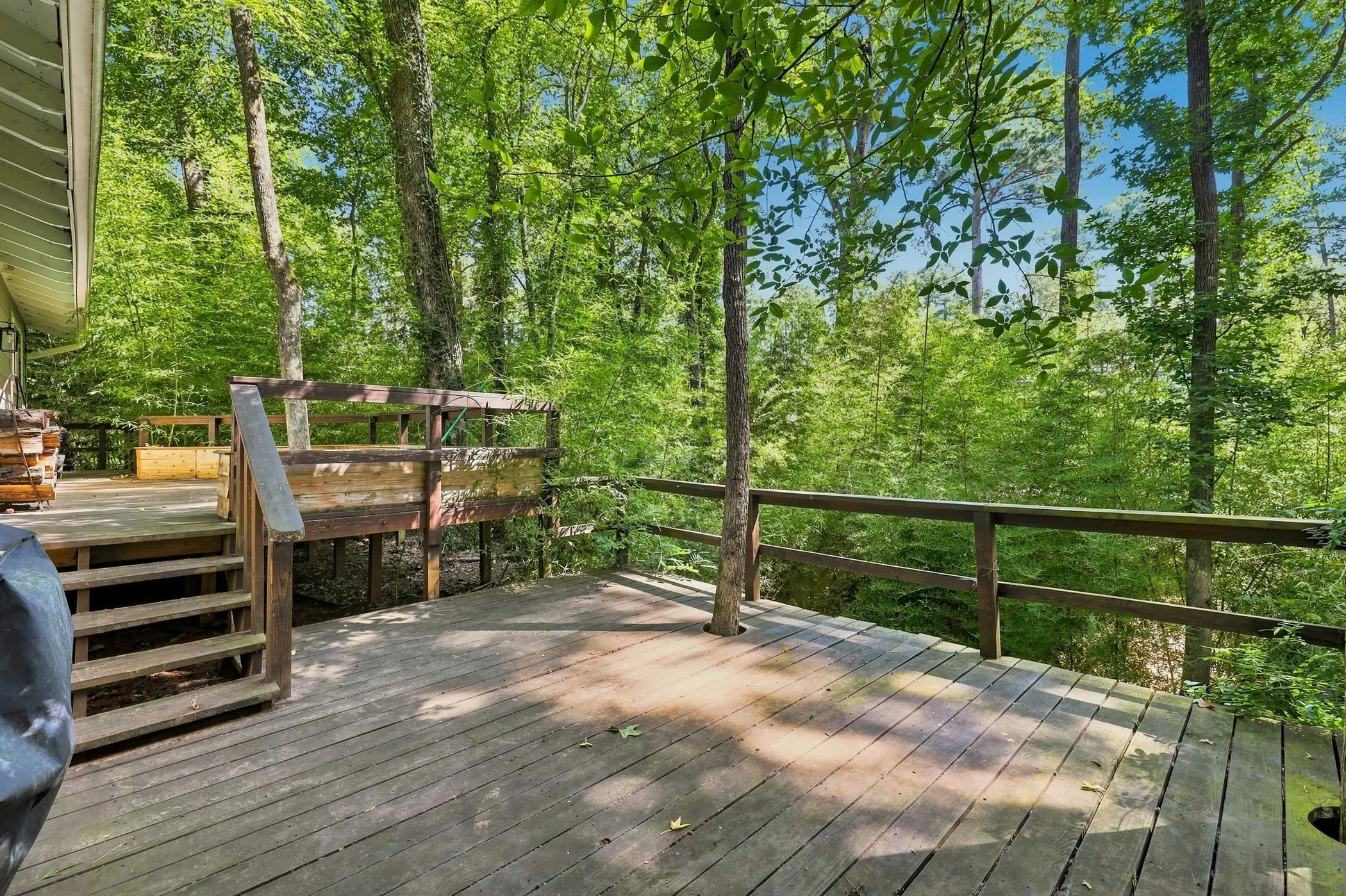 Spacious wood deck with natural wood railing, integrated tree feature, and steps leading to an additional deck area