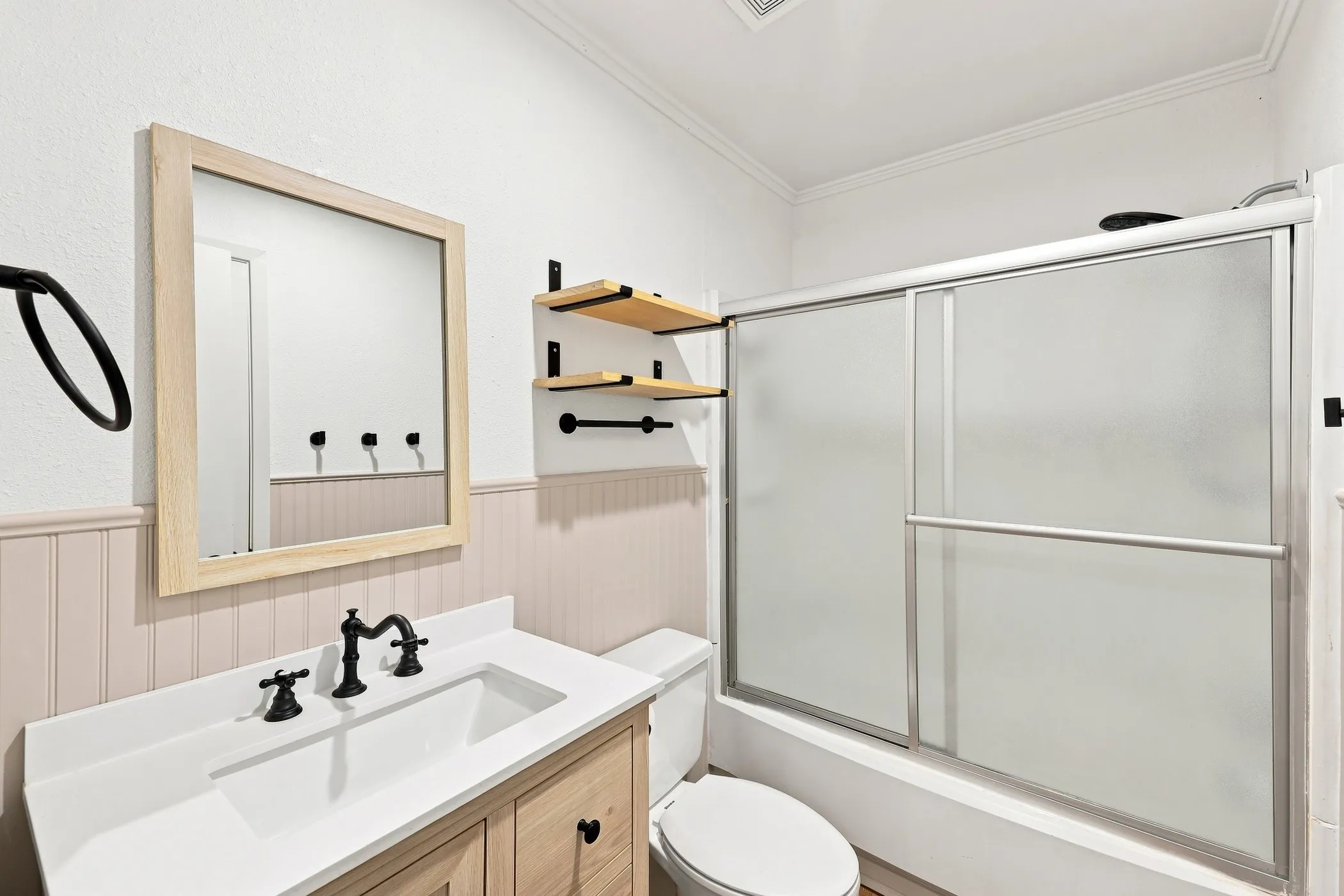 Bathroom featuring a wood-finish vanity with a single basin, a framed mirror, and matte black fixtures