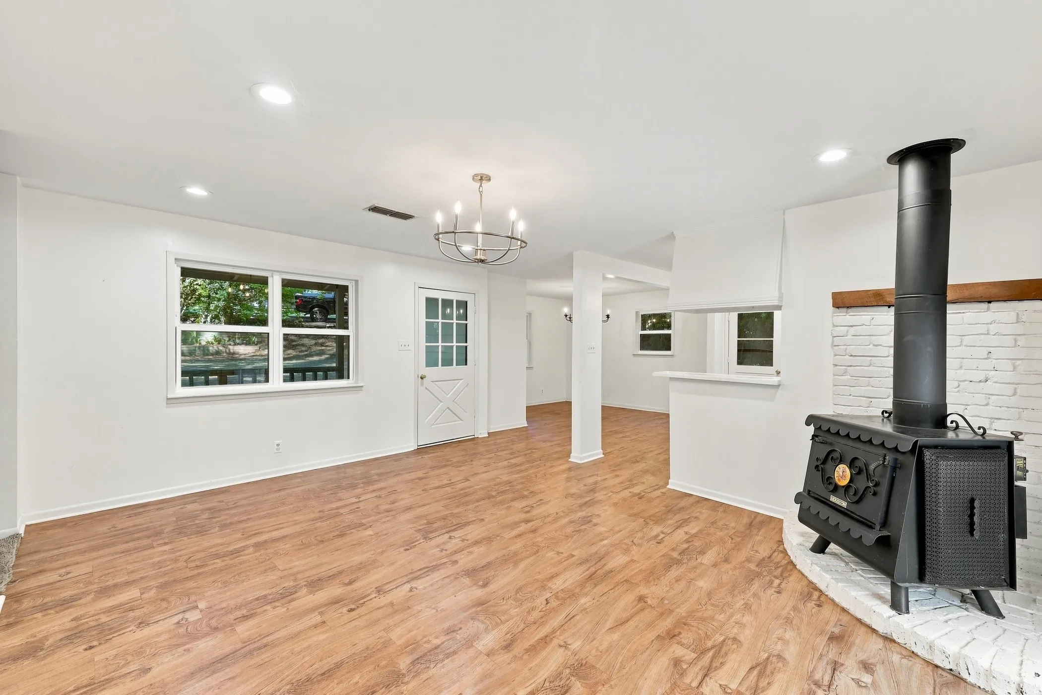 Spacious living area featuring wood-finish flooring, a traditional wood-burning stove with a painted brick hearth, and recessed lighting