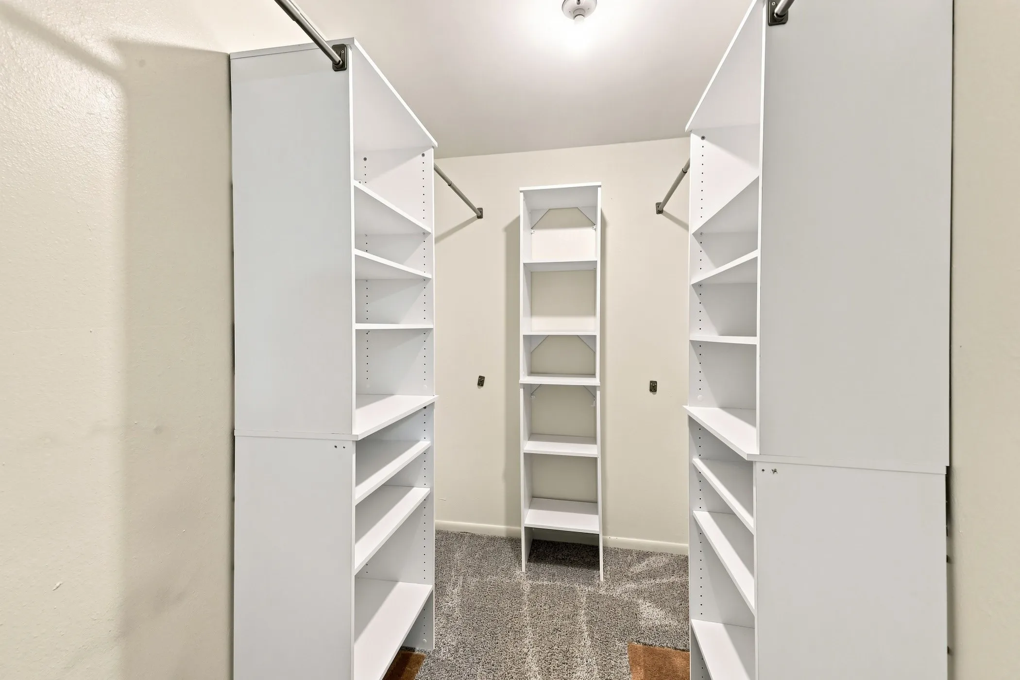 Walk-in closet featuring built-in white shelving units, hanging rods, and light beige walls