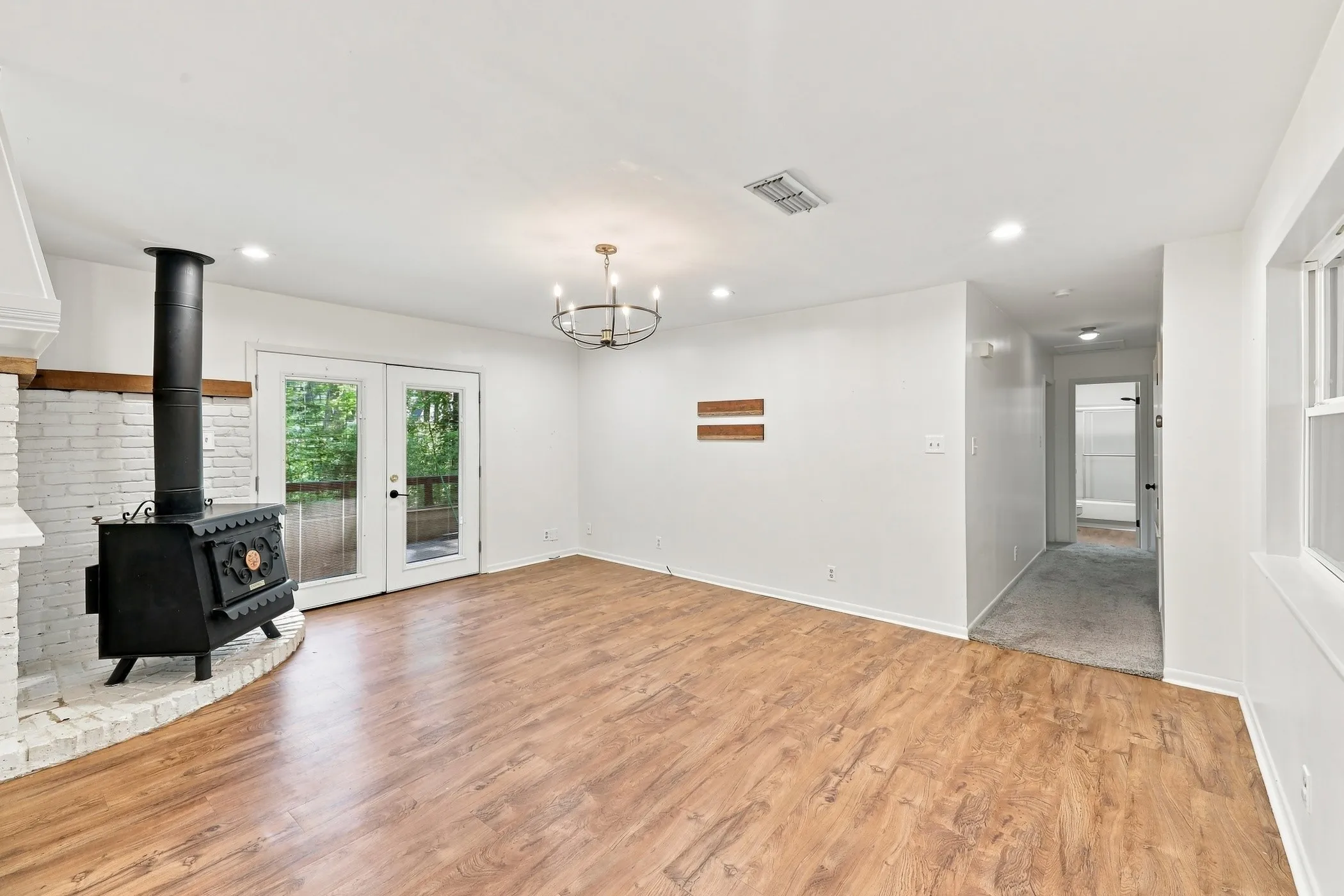 Living area featuring wood-finish flooring, a white brick fireplace with a wood-burning stove, and double glass doors