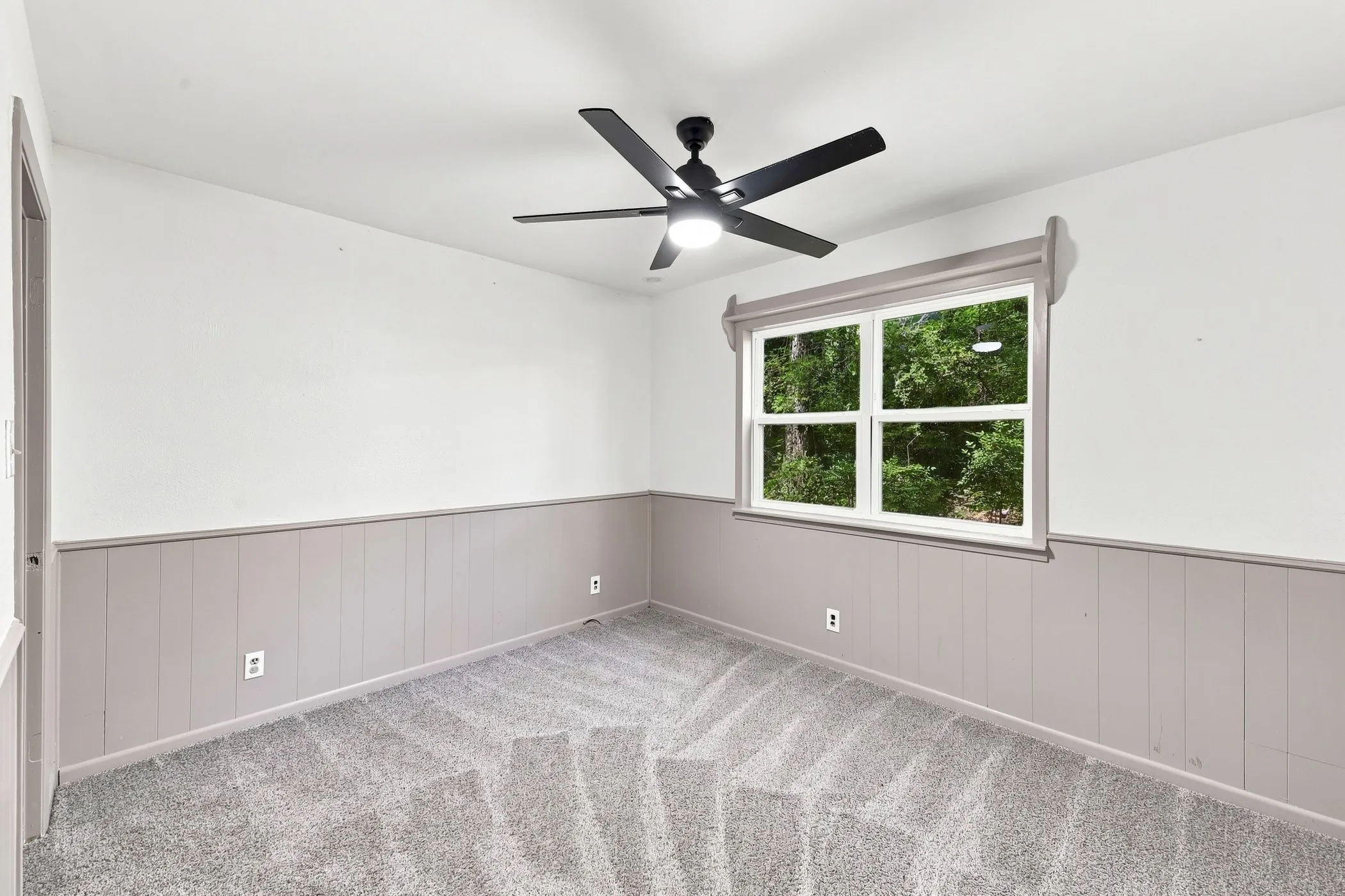 Room featuring light grey carpeting, white upper walls, and grey vertical panel wainscoting