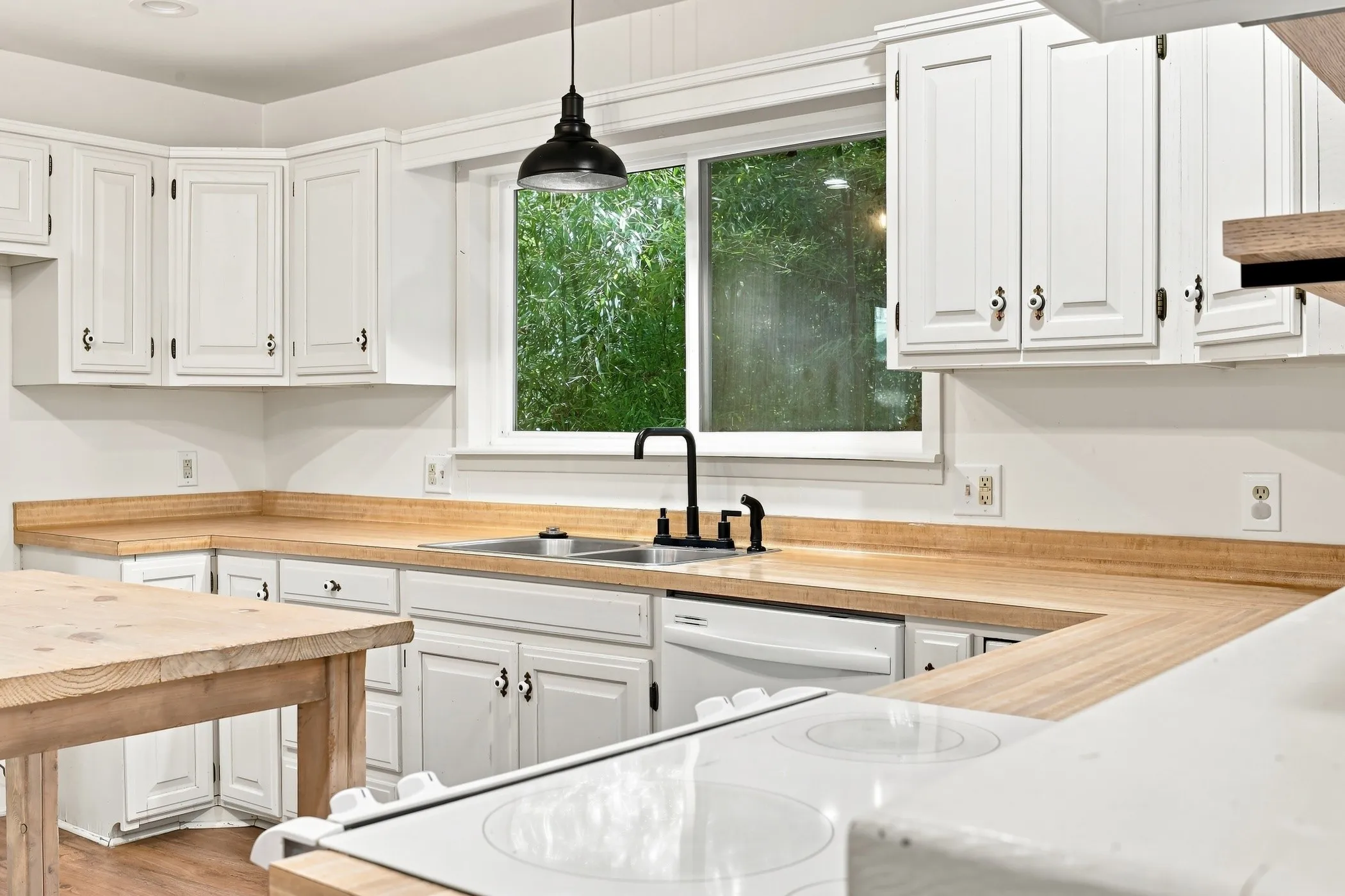 Kitchen featuring white cabinetry with dark hardware, wood-finish countertops, and a stainless steel sink with a matte black faucet