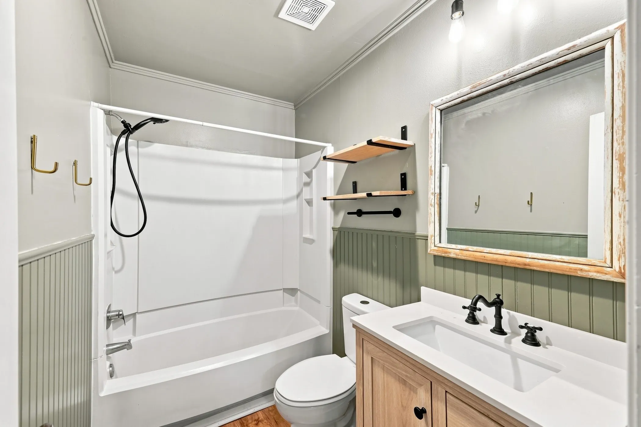 Bathroom featuring a white tub/shower combination, beadboard wainscoting, and wood-finish flooring