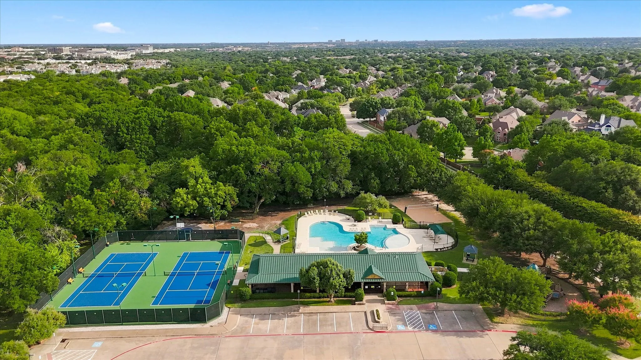 Expansive community grounds featuring twin tennis courts, a large swimming pool, a dedicated clubhouse building, and a spacious parking area