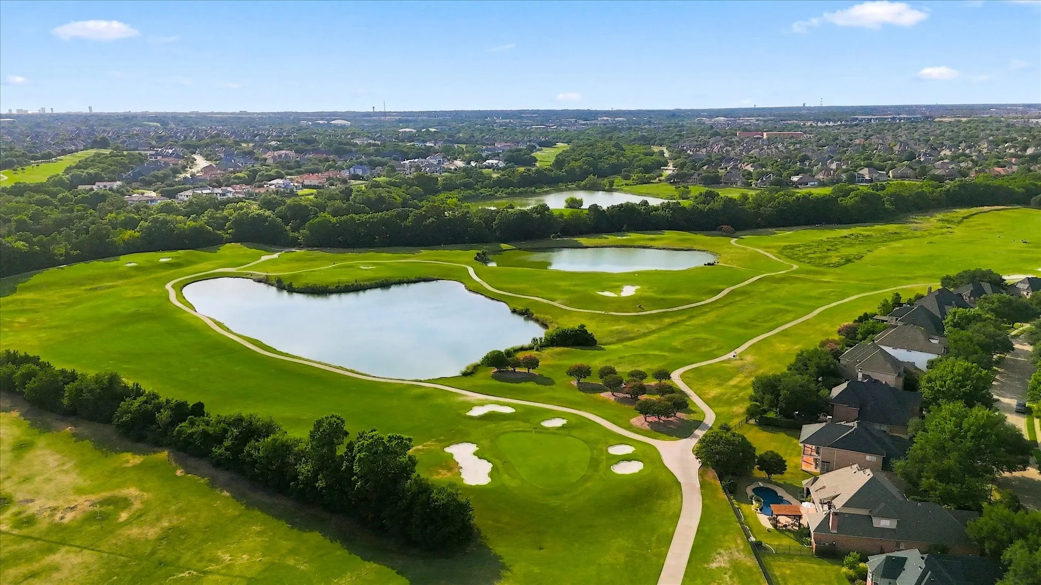Expansive golf course setting featuring multiple water features, manicured greens, and paved cart paths