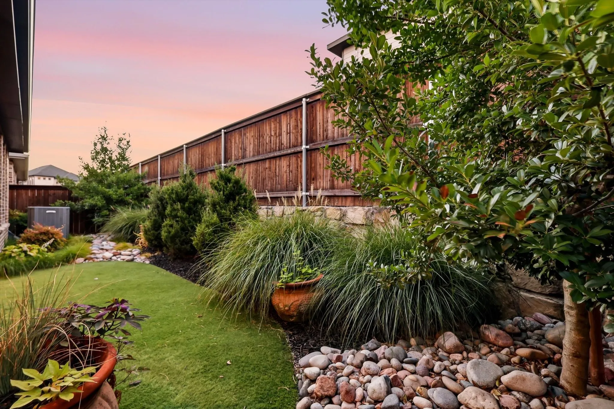 Landscaped backyard featuring a manicured lawn, established shrubs, and a decorative rock bed
