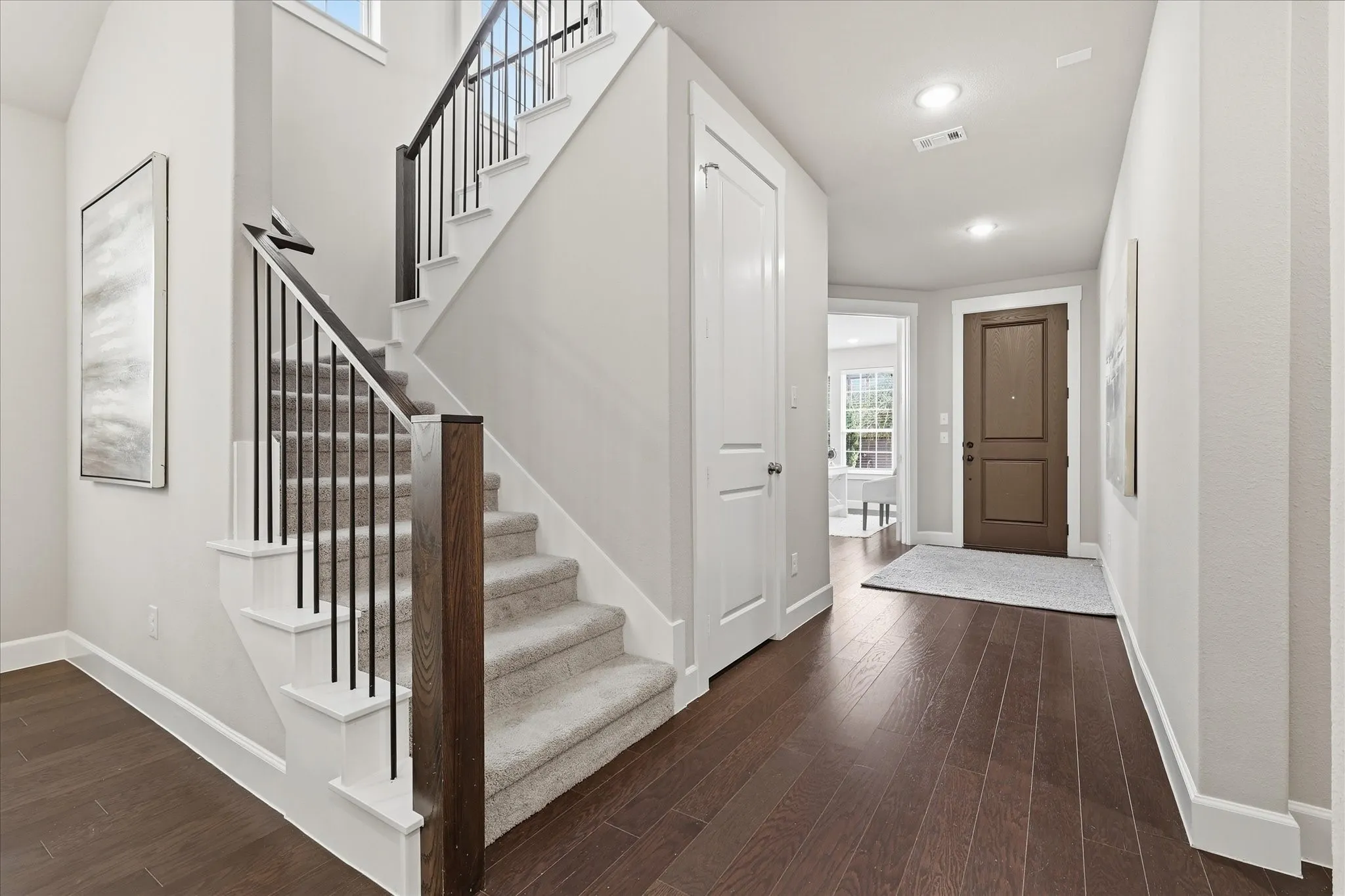 Wood-finish flooring, staircase with dark wood newel post and metal balusters, recessed lighting, and white interior doors