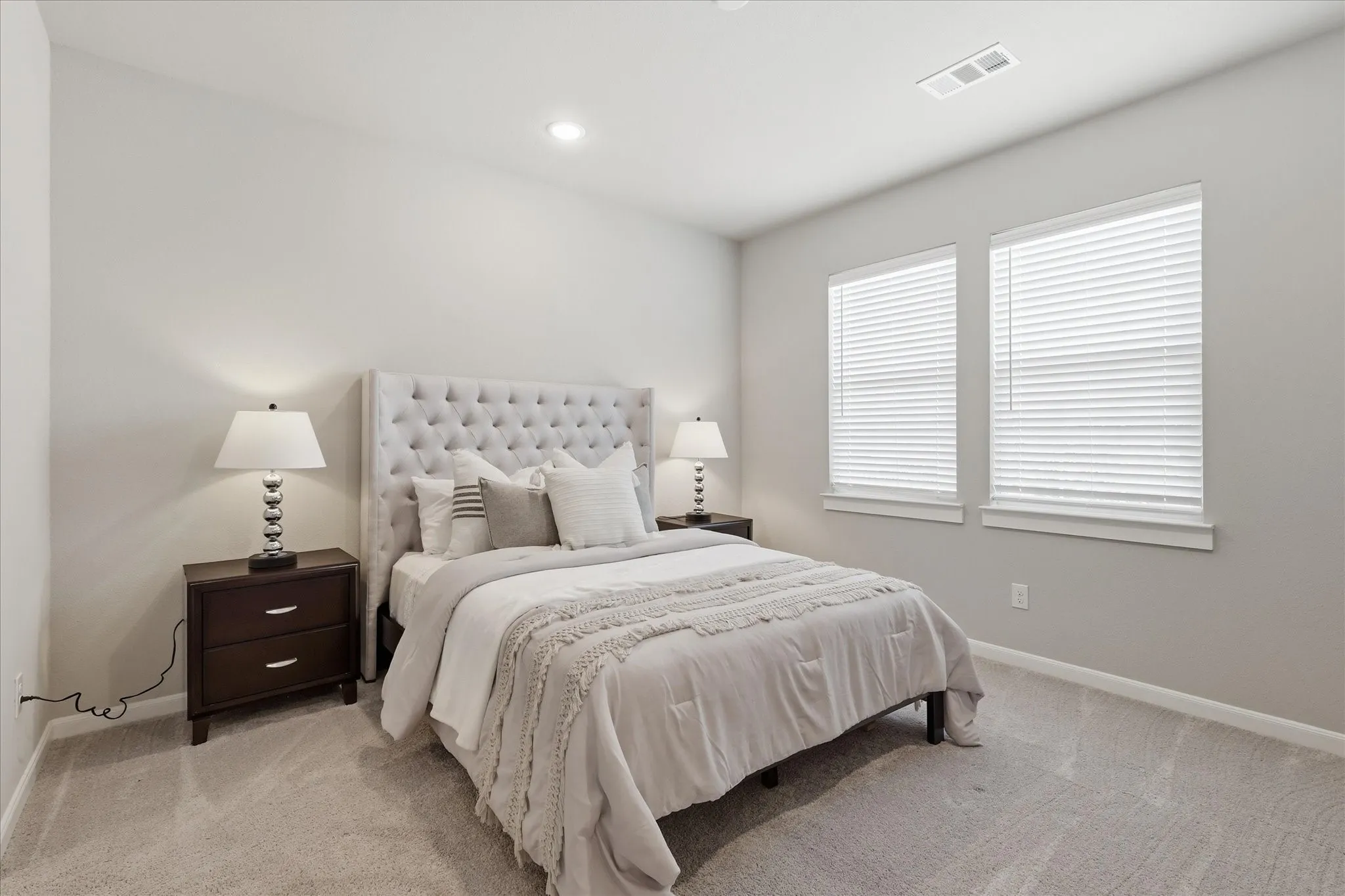 Recessed lighting, two windows with blinds, light-toned carpeting, and light gray wall paint