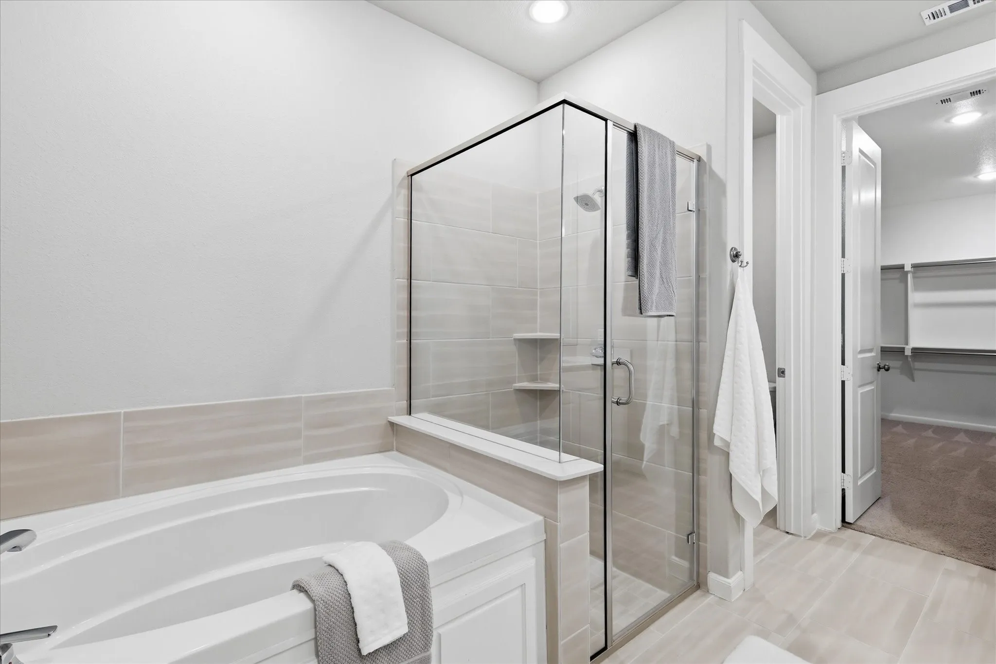 Built-in soaking tub, glass-enclosed shower with tiled walls, integrated shower shelving, and neutral tile flooring