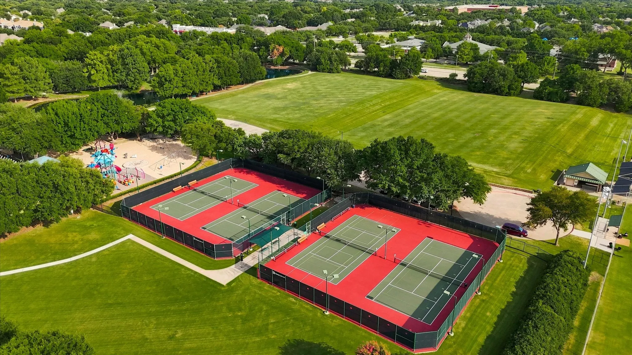 Manicured grounds featuring multiple tennis courts, expansive green spaces, and a dedicated playground area