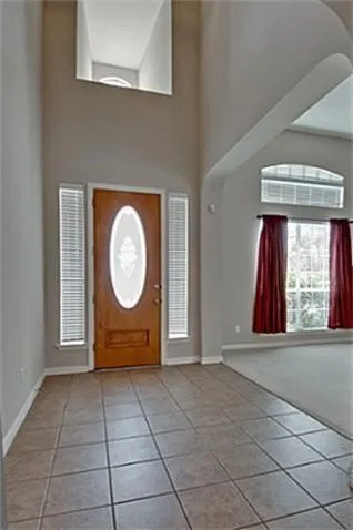 Entry featuring a two-story ceiling, a wood-finish door with an oval glass insert, and side light windows
