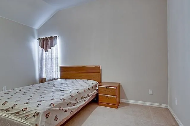 Room with a vaulted ceiling, neutral wall paint, and beige carpet flooring