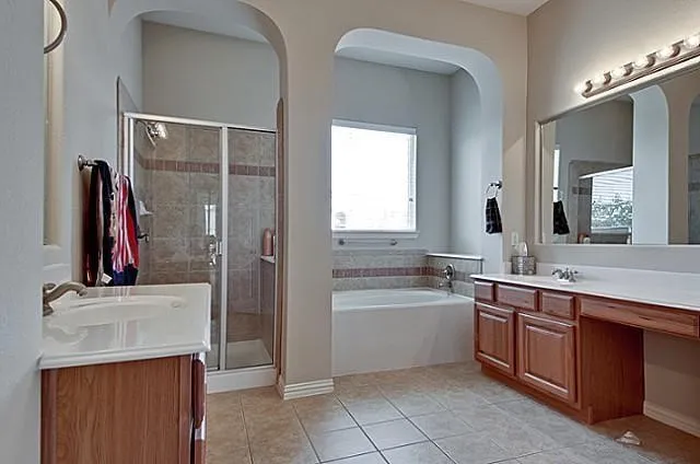 Full bathroom featuring a walk-in shower with glass enclosure, a built-in bathtub with tiled surround, a long vanity with wood-finish cabinetry, dual sinks, and tile flooring