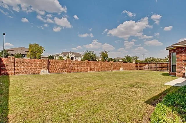Expansive backyard featuring a manicured lawn, a full brick perimeter fence, a section of wood privacy fencing, and a brick-clad exterior