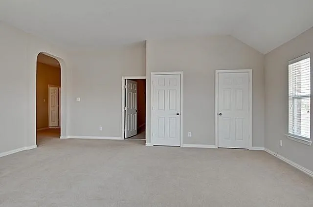 Spacious primary bedroom featuring neutral carpeting, multiple closet spaces with white six-panel doors, and abundant natural light from large windows with plantation shutters