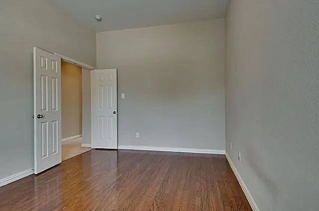 Room featuring wood-finish flooring, two panel-style doors, light-toned wall paint, and white baseboards