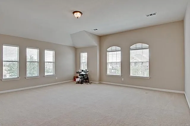 Spacious room featuring neutral carpeting, light-toned wall paint, and multiple windows with blinds