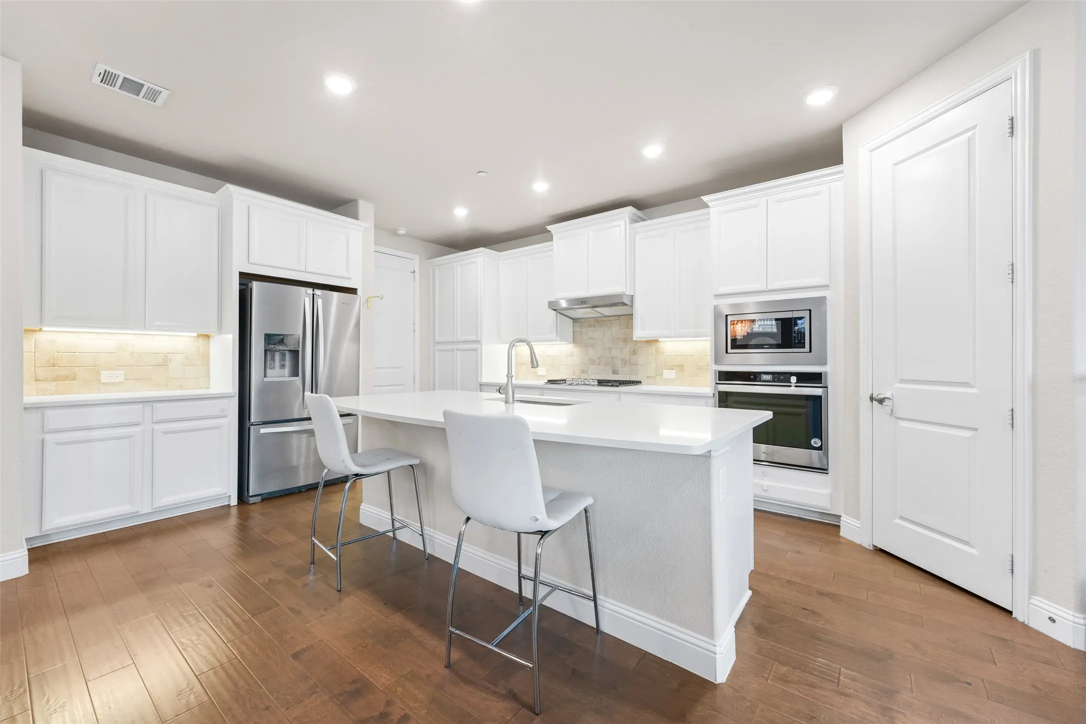 Kitchen featuring a large island with seating, white shaker cabinetry, stainless steel appliances, and wood-finish flooring
